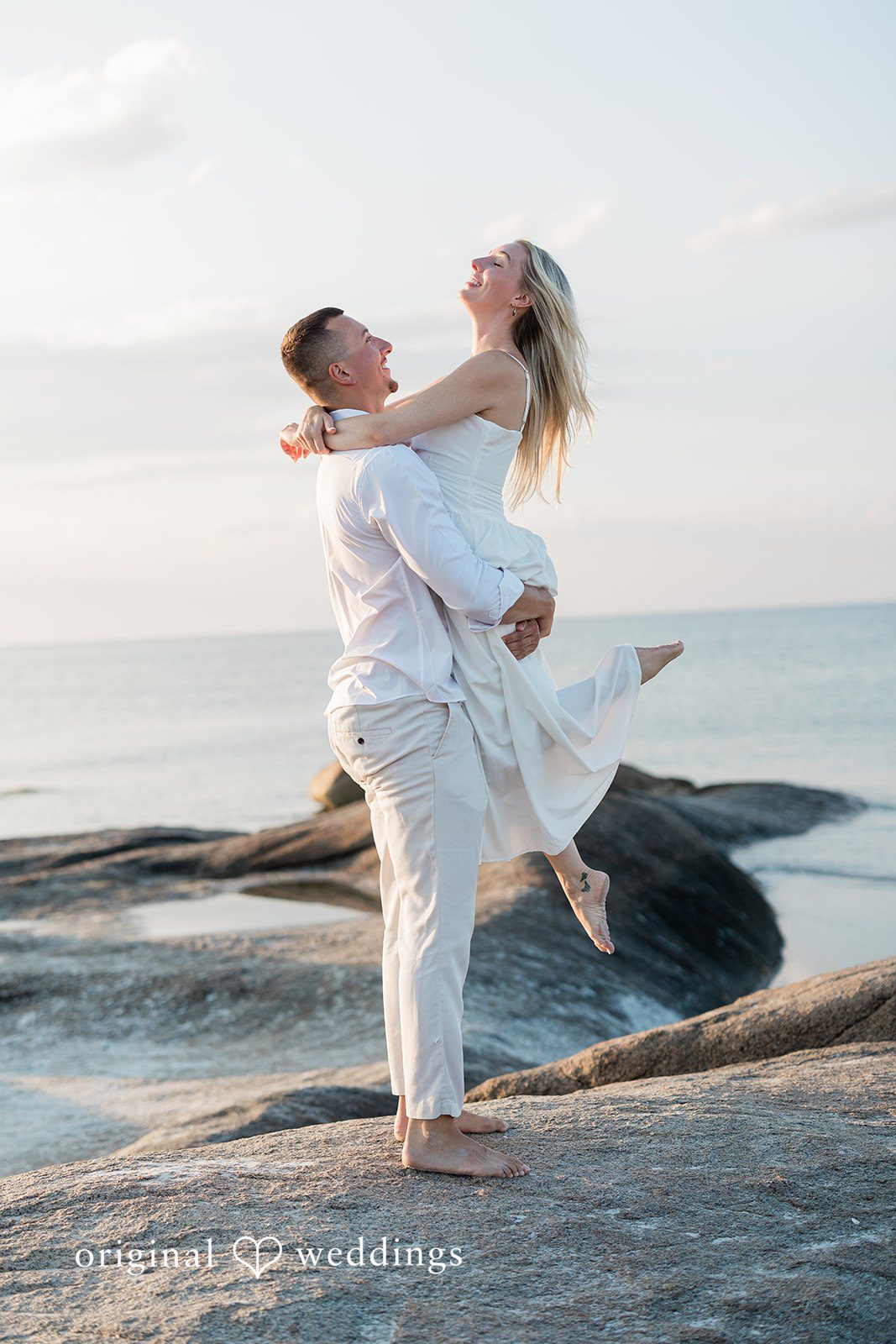 A man lifting a woman joyfully in the air on a beach.