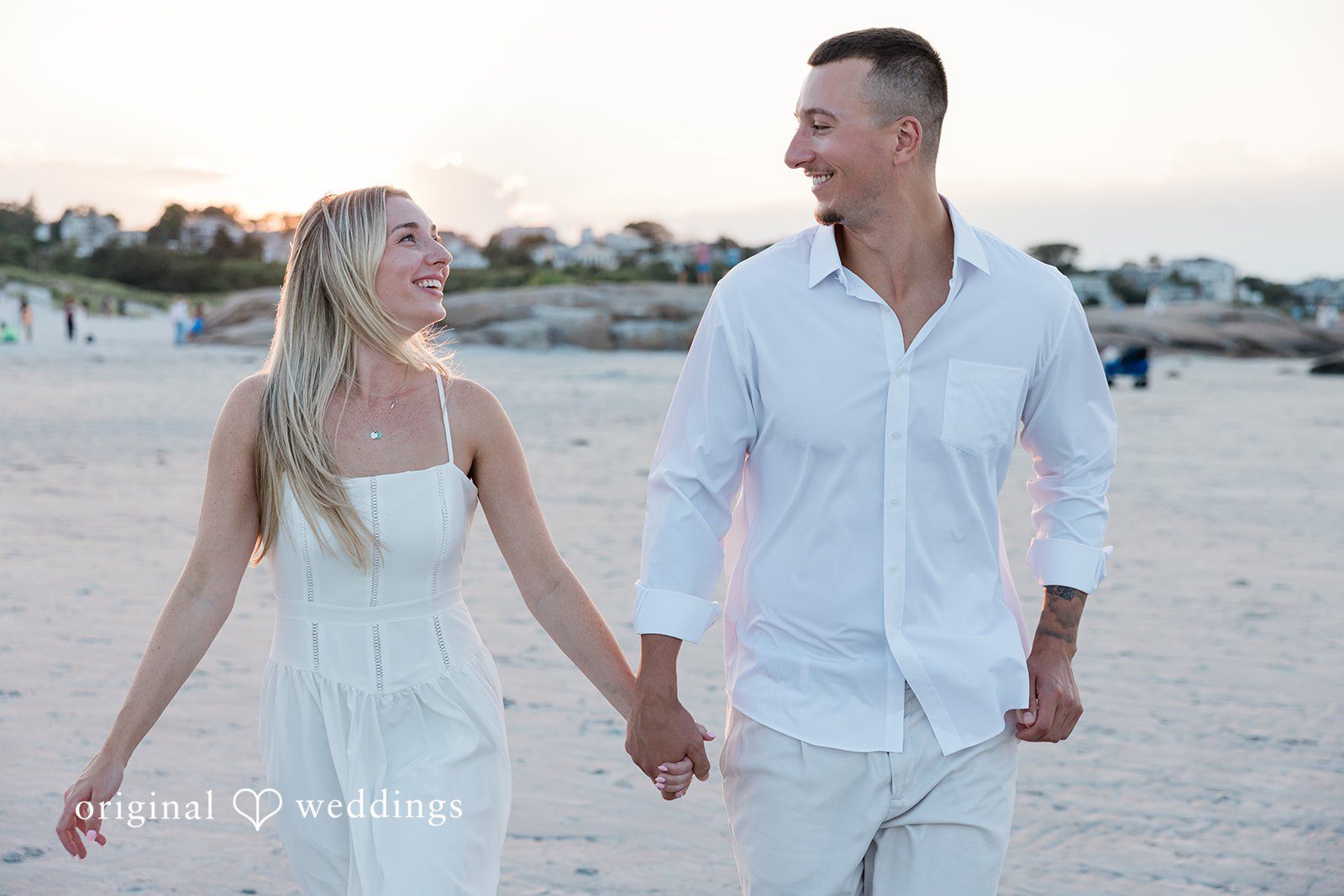 A couple dressed in white holding hands while walking through a field.