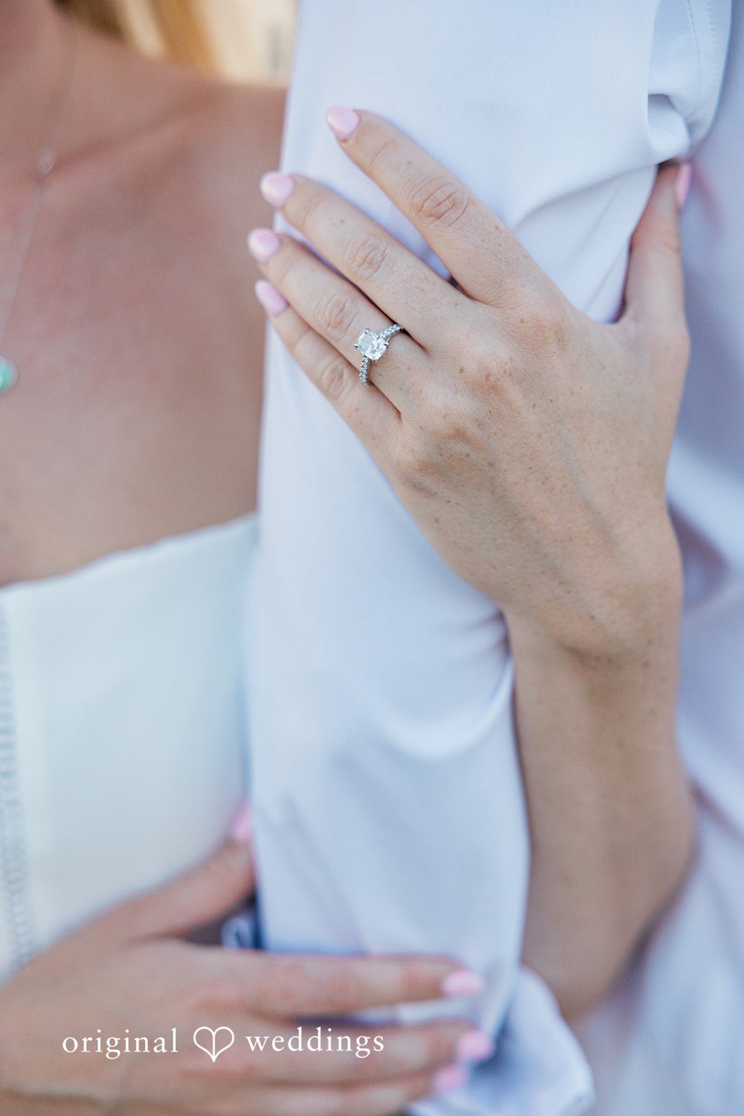 A close-up shot showing a woman's hand with an engagement ring resting on a man's chest.