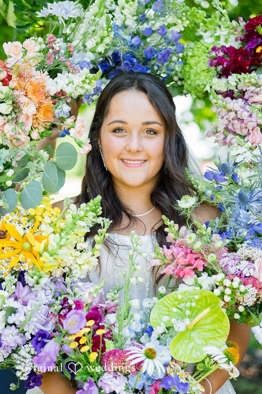 Melayna + Harley A smiling bride is framed by a colorful wreath of flowers.