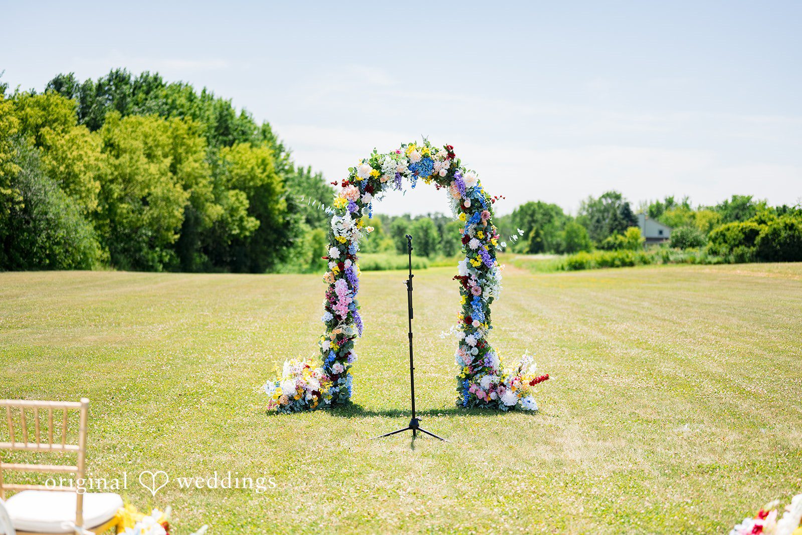 Melayna + Harley A floral wedding arch stands on a green grassy lawn.
