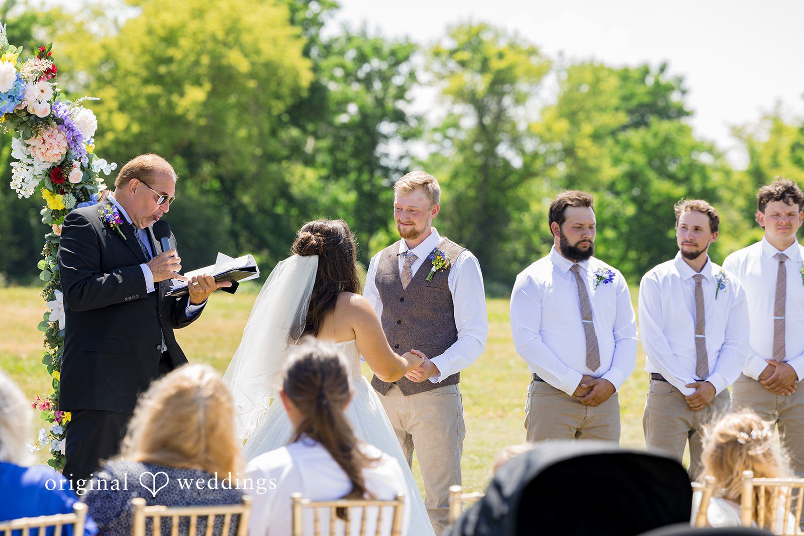 Melayna + Harley A wedding ceremony takes place under a large shade tree.