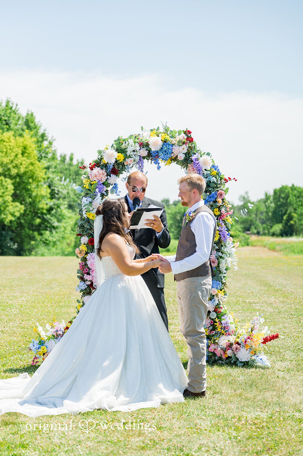 Melayna + Harley A bride and groom stand together before a floral arch.