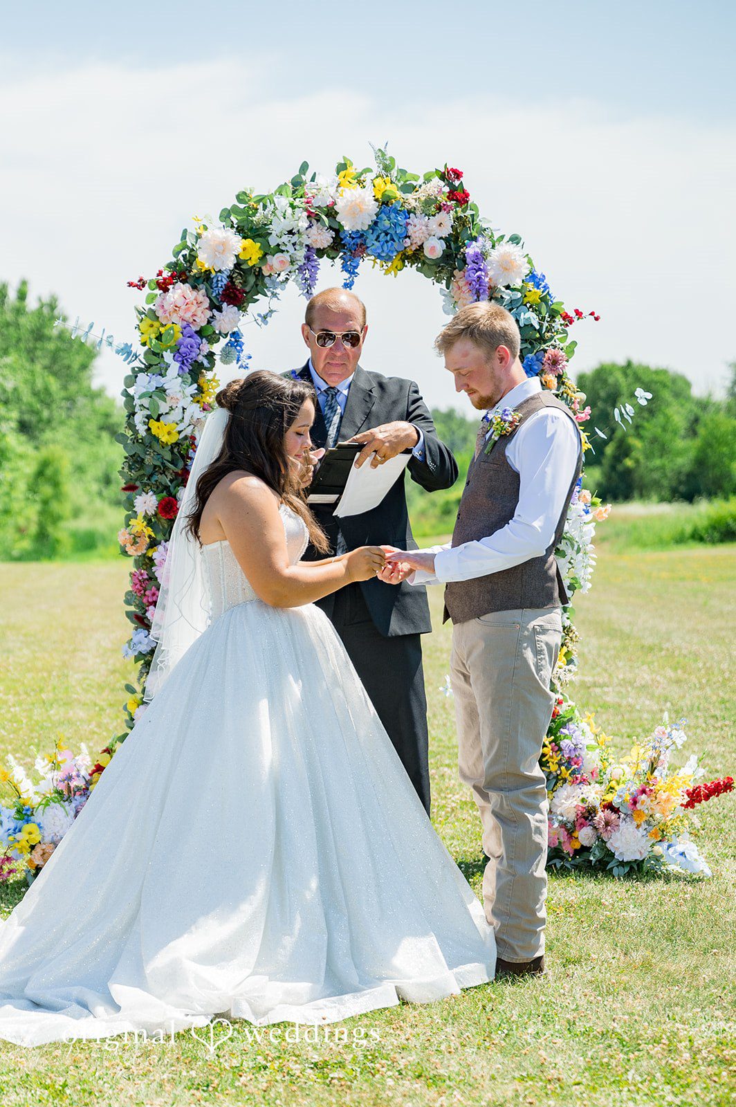 Melayna + Harley A bride and groom exchange vows under a circular floral arch.