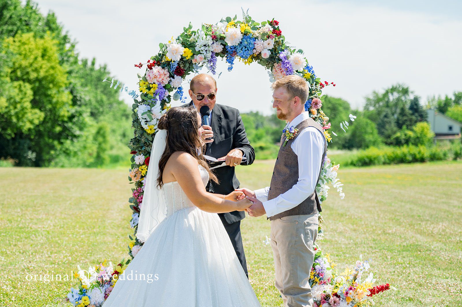 Melayna + Harley A bride and groom exchange vows under a colorful floral arch.