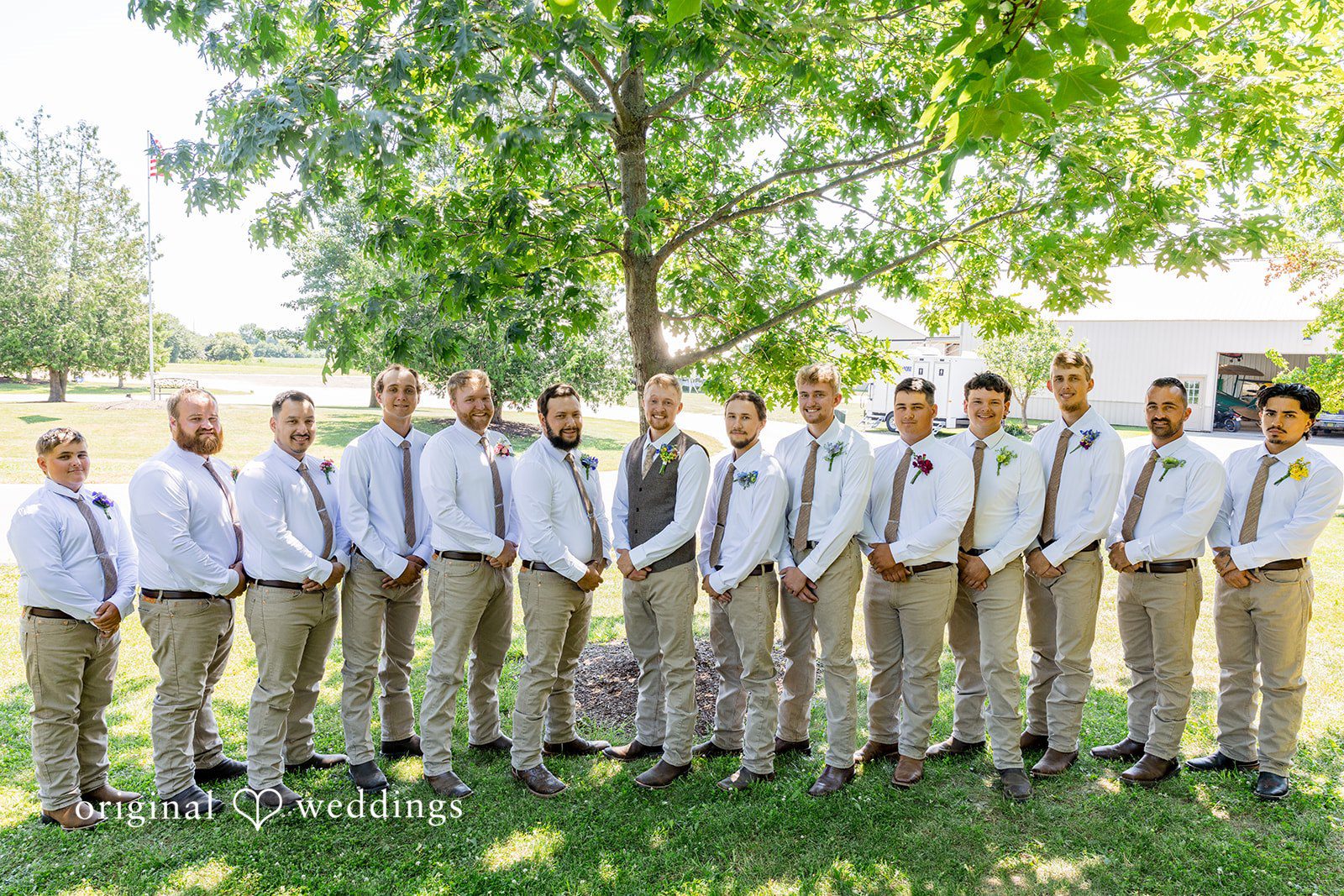 Melayna + Harley A row of groomsmen in matching vests and trousers stand together.