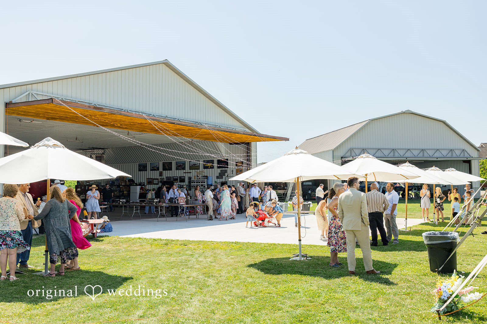 Melayna + Harley Guests gather for a reception near an open-sided white barn.