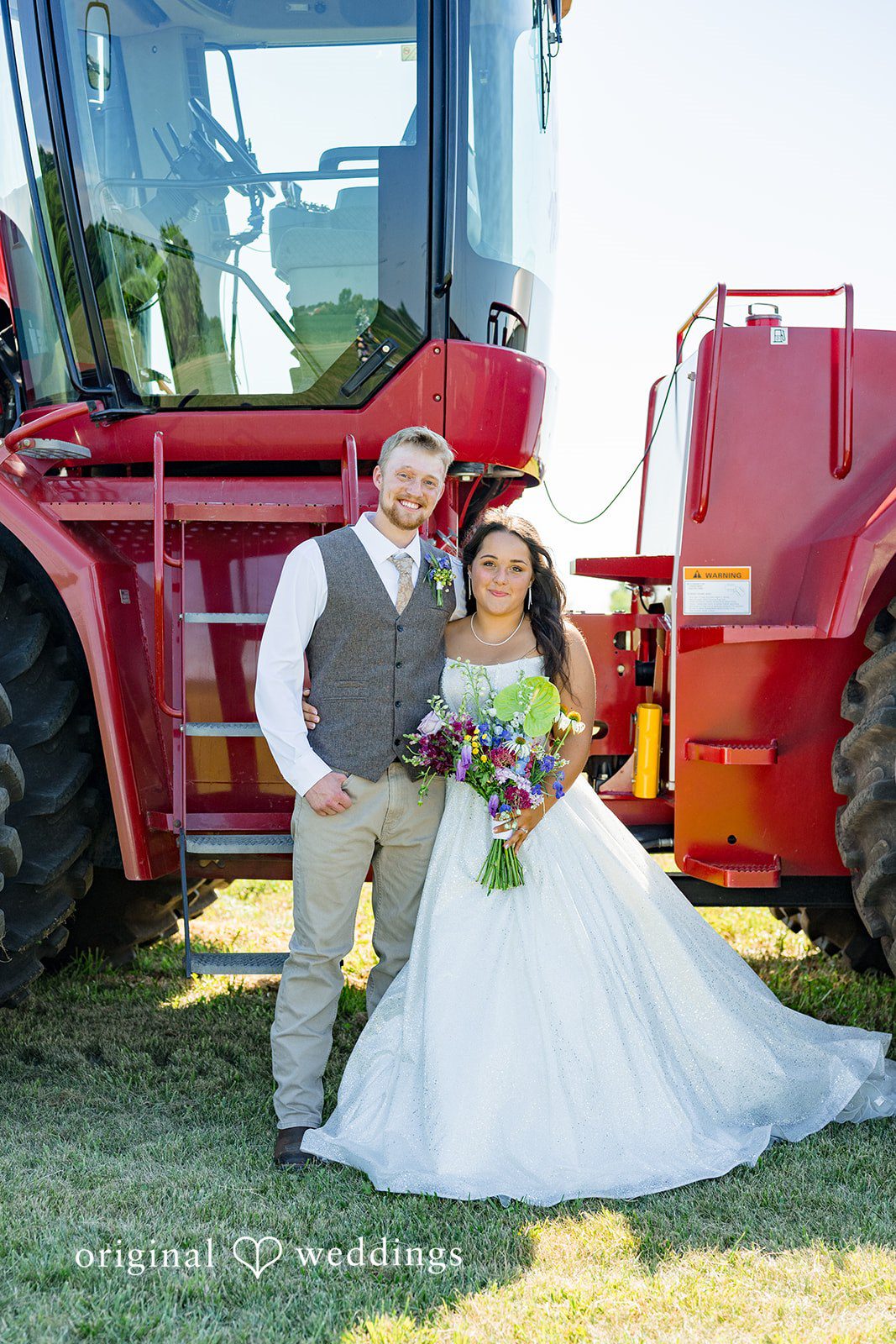 Melayna + Harley A bride and groom pose together in front of a red tractor.