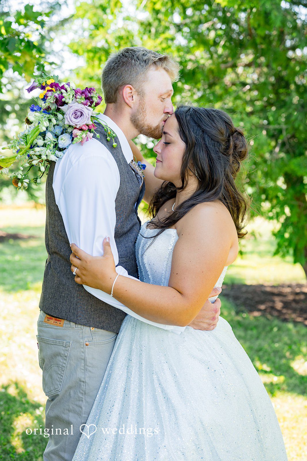 Melayna + Harley A groom embraces his bride from behind in a grassy field.
