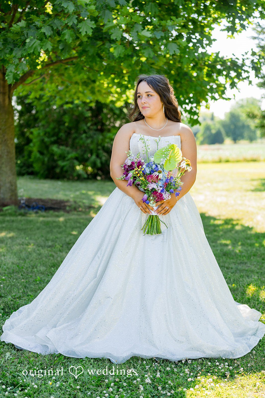 Melayna + Harley A bride poses on a grassy field holding her bouquet.