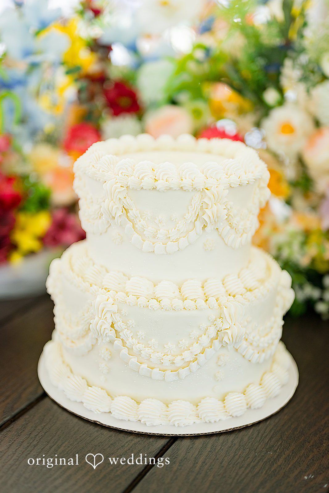 Melayna + Harley A three-tiered white wedding cake features textured frosting.
