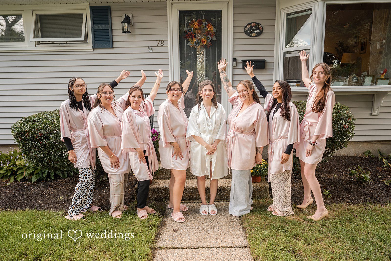 Emily + Angelo Group of bridesmaids in matching light pink dresses posing outside a house.