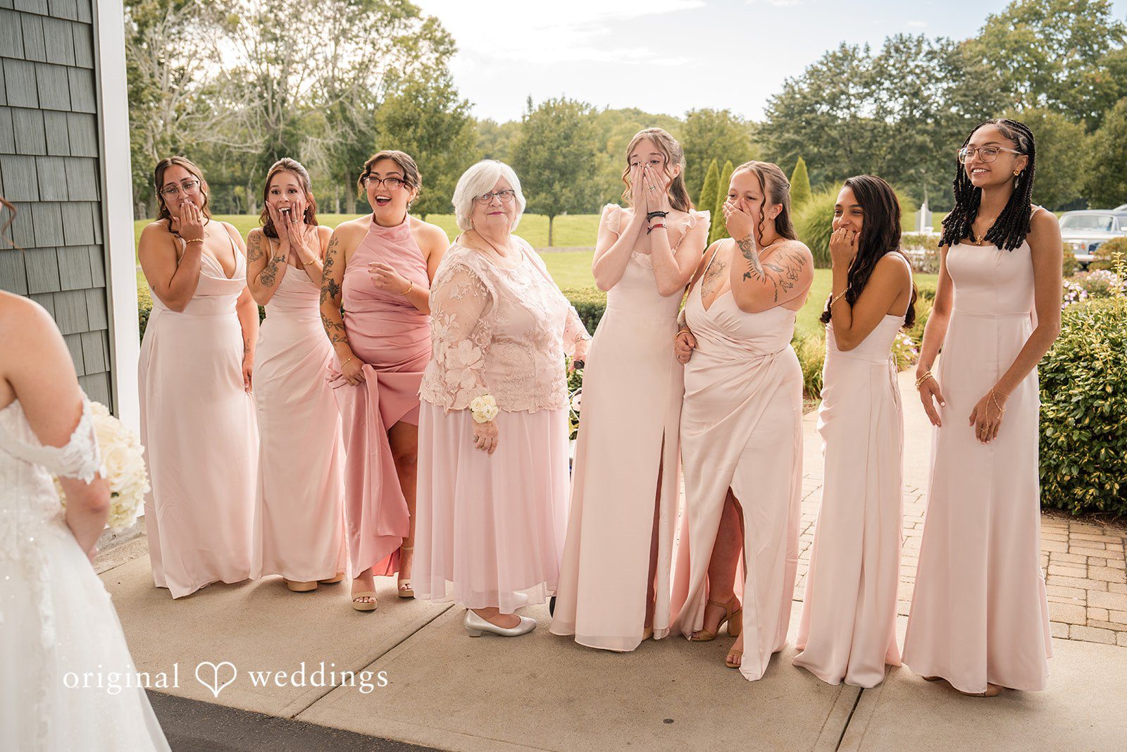 Emily + Angelo Group of bridesmaids standing side-by-side in matching floor-length pink gowns.