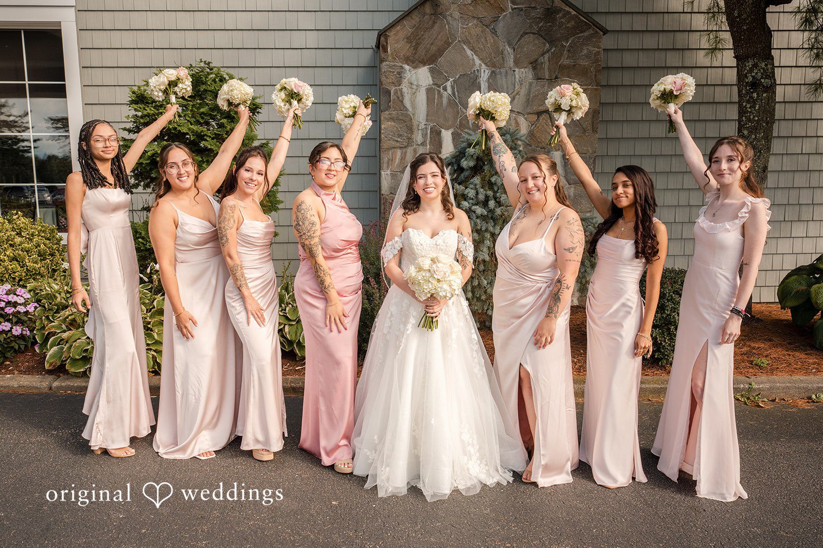 Emily + Angelo Group of bridesmaids cheerfully holding up their matching pink dresses while posing in a row.