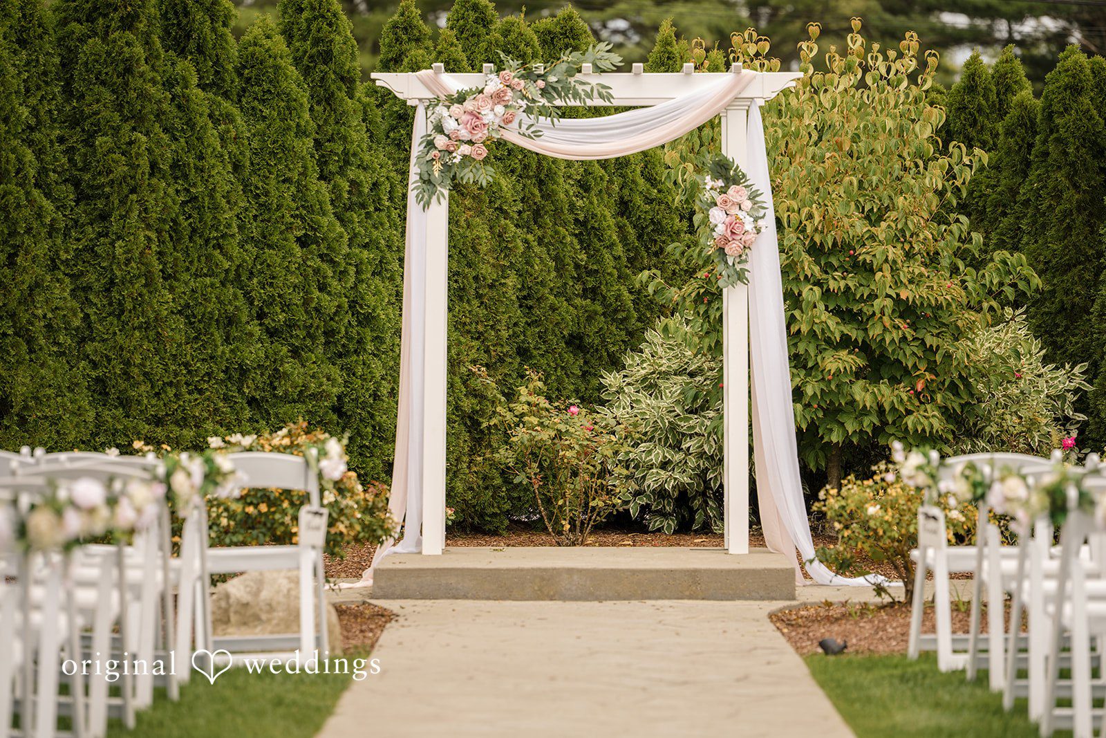 Emily + Angelo White wedding altar arch decorated with draped fabric on a manicured lawn.