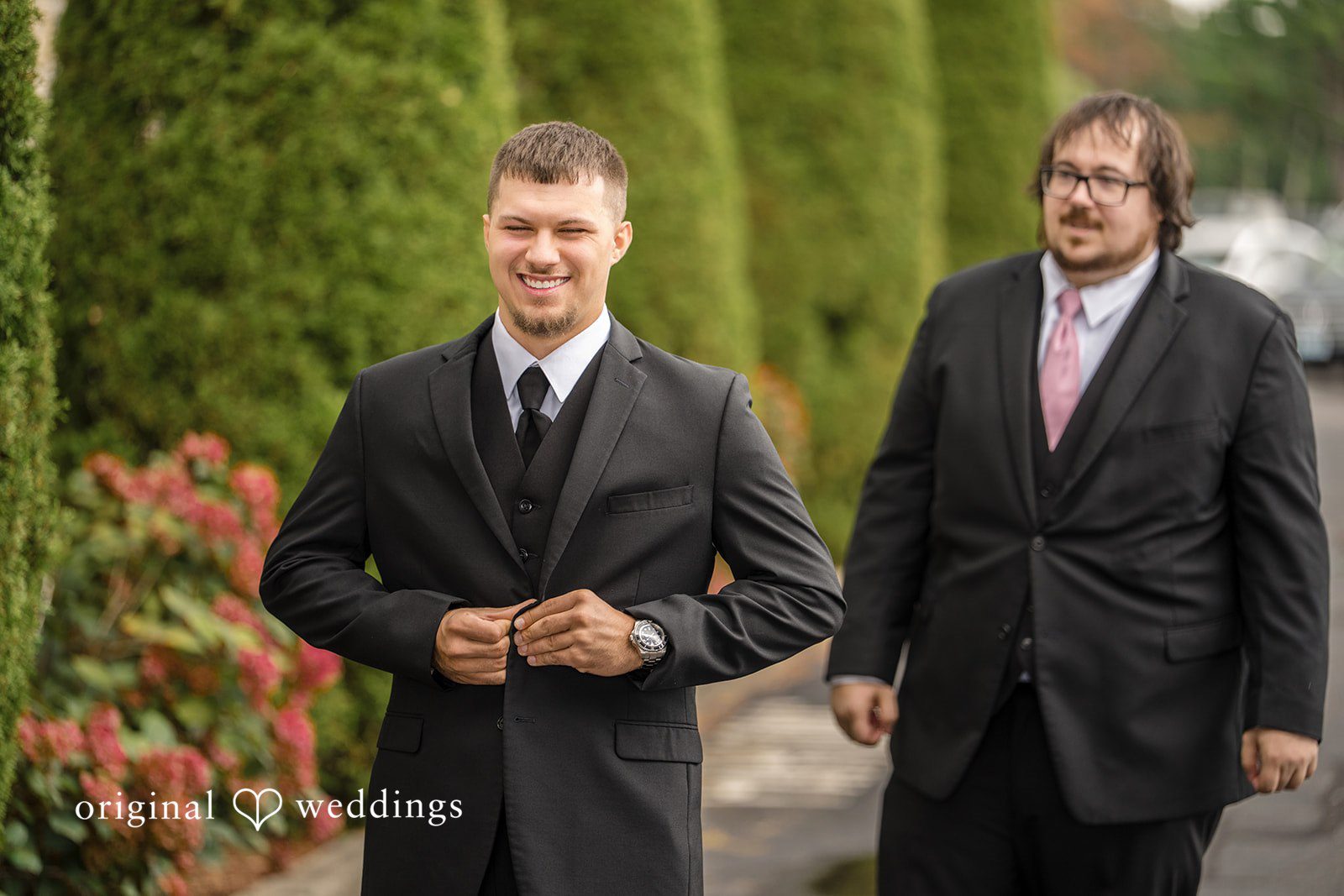 Emily + Angelo Groom and groomsman dressed in matching black suits standing next to each other.