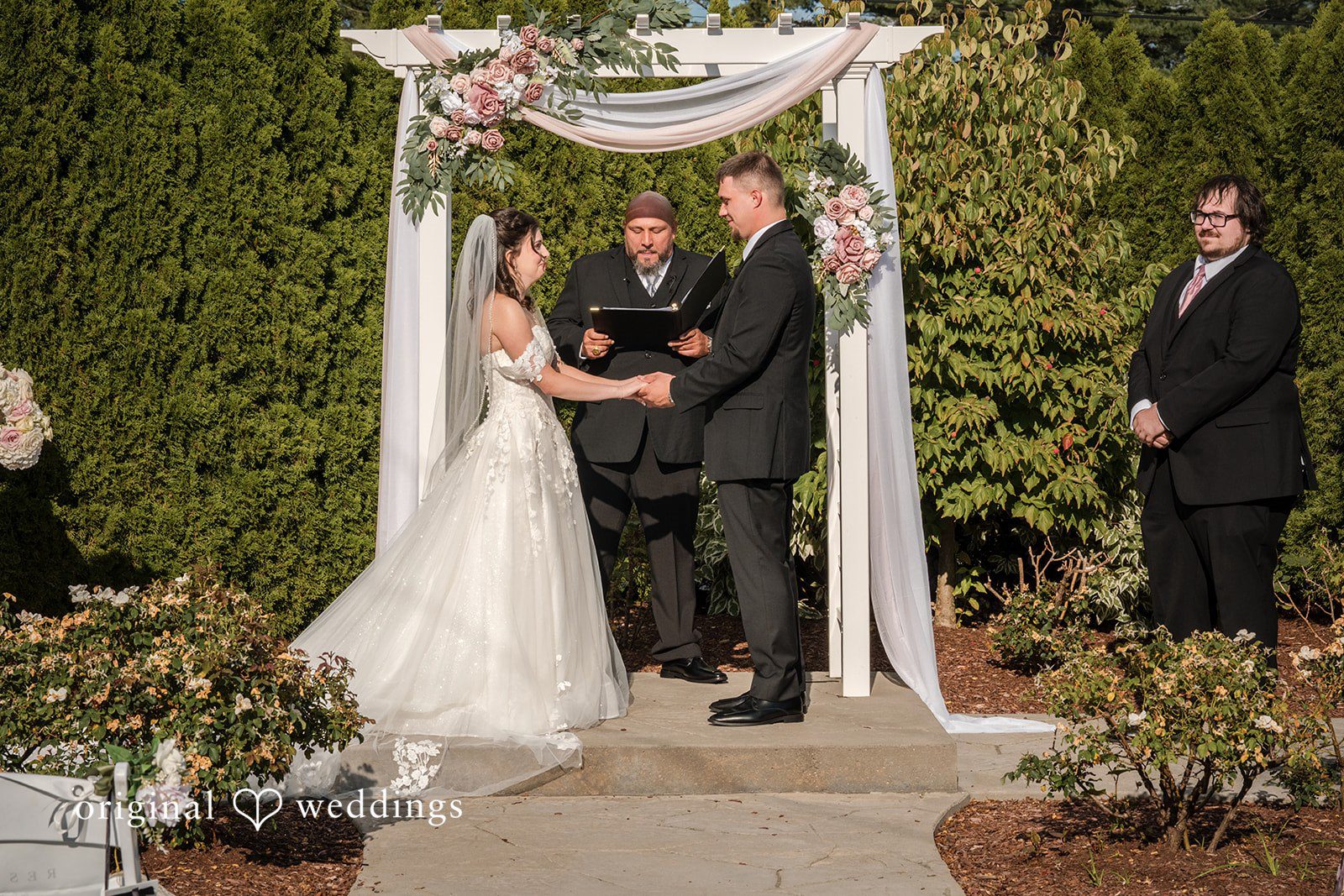 Emily + Angelo Bride in a white gown and veil walking down an aisle under a white fabric canopy.