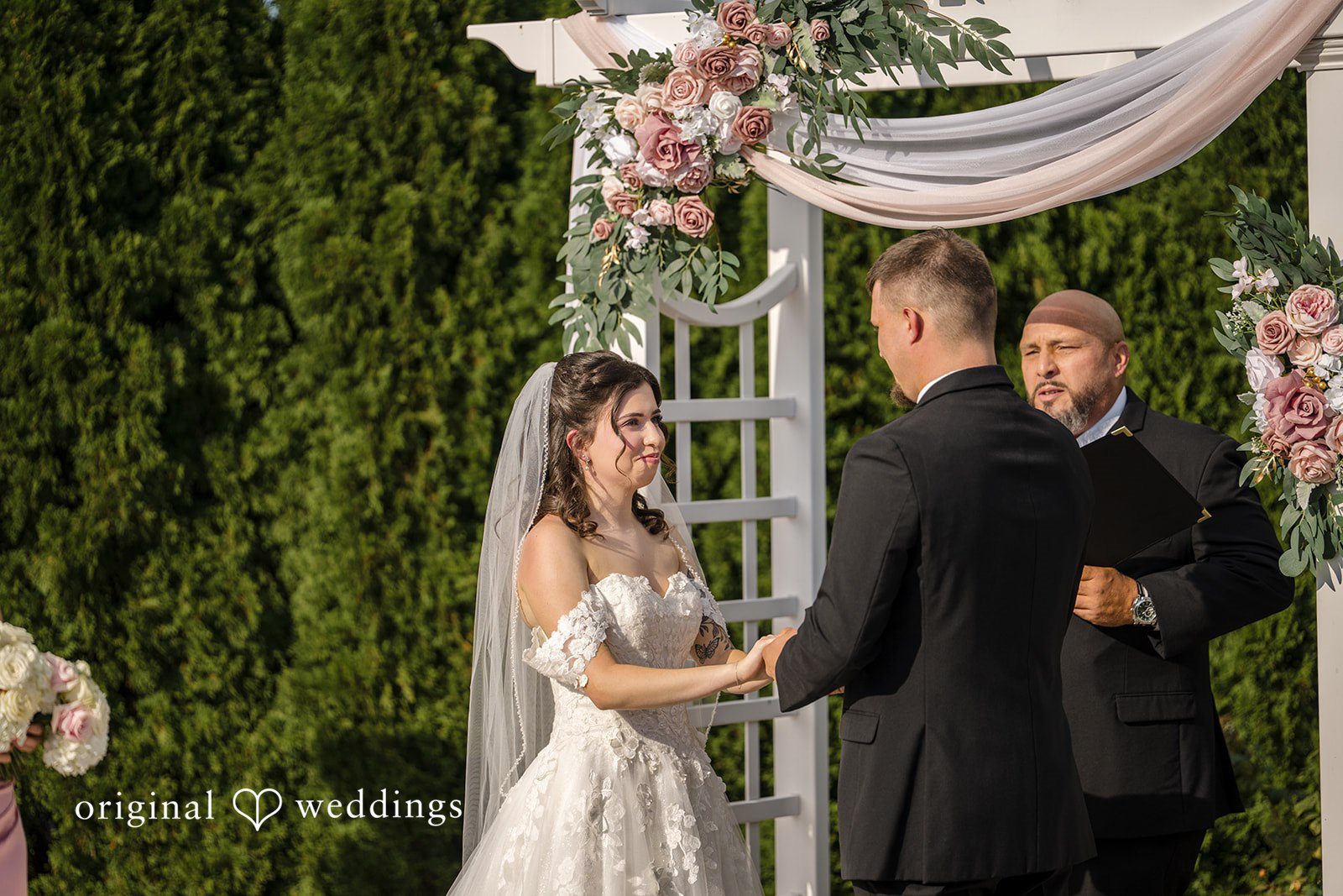 Emily + Angelo Bride and groom standing together beneath a decorated wedding arch during the ceremony.