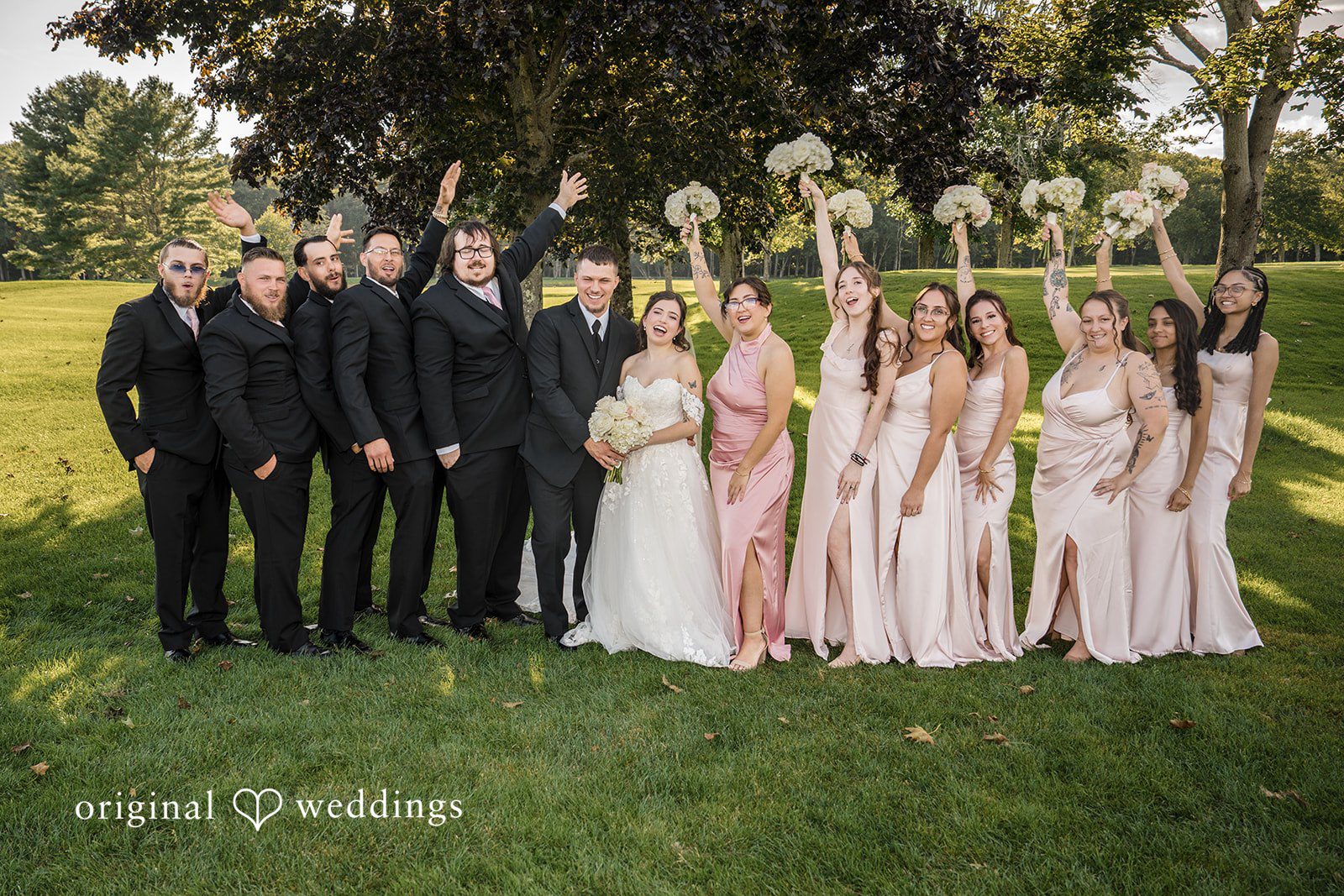 Emily + Angelo Wedding party posing together on a manicured green lawn.
