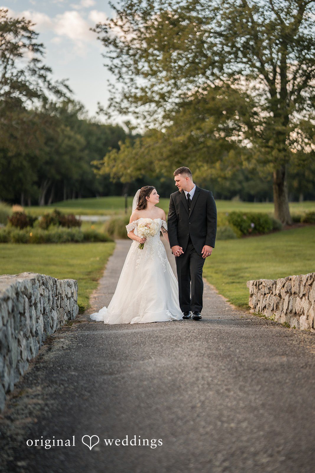 Emily + Angelo Bride and groom walking together down a pathway surrounded by trees.