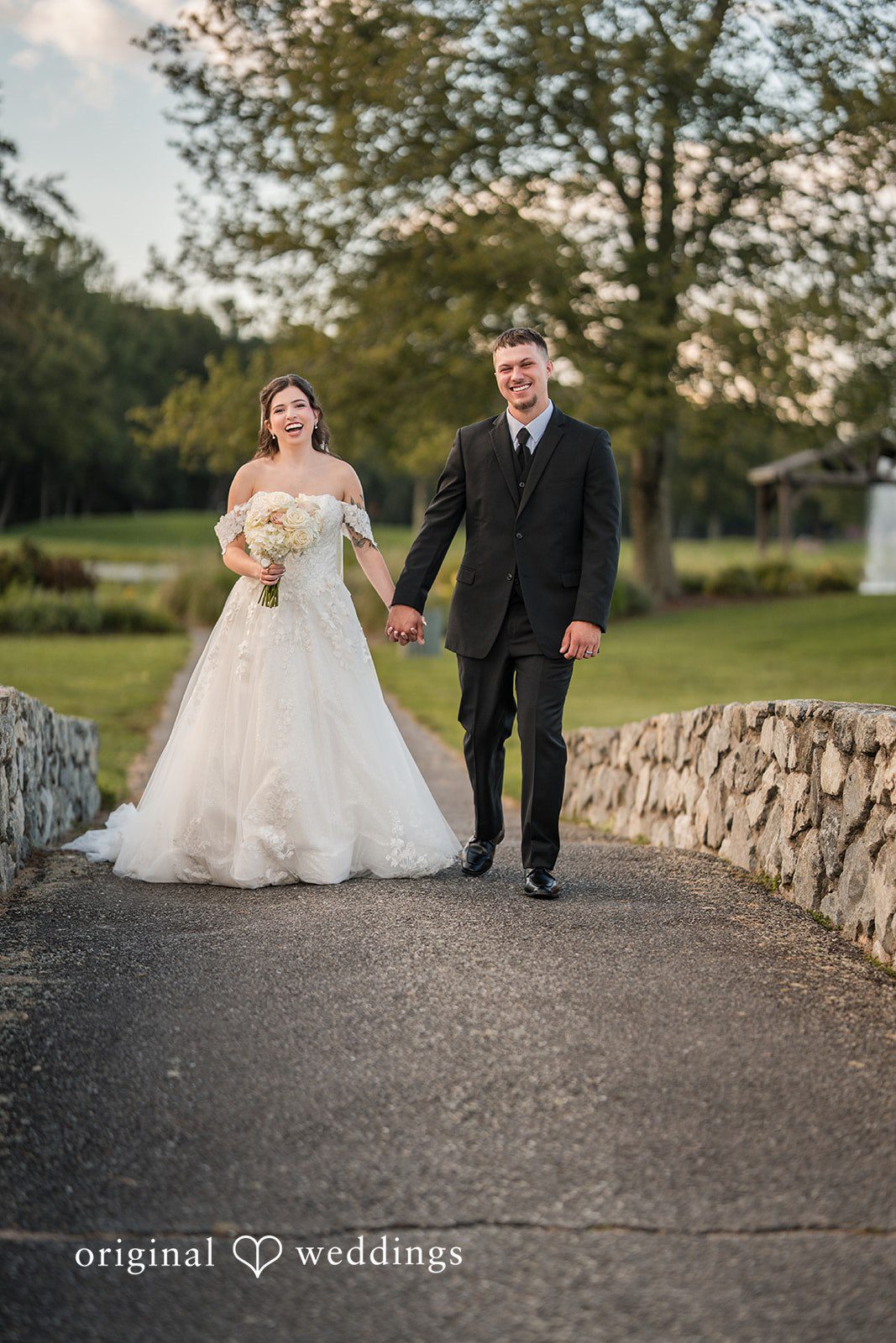 Emily + Angelo Bride and groom walking hand-in-hand across a small stone bridge.