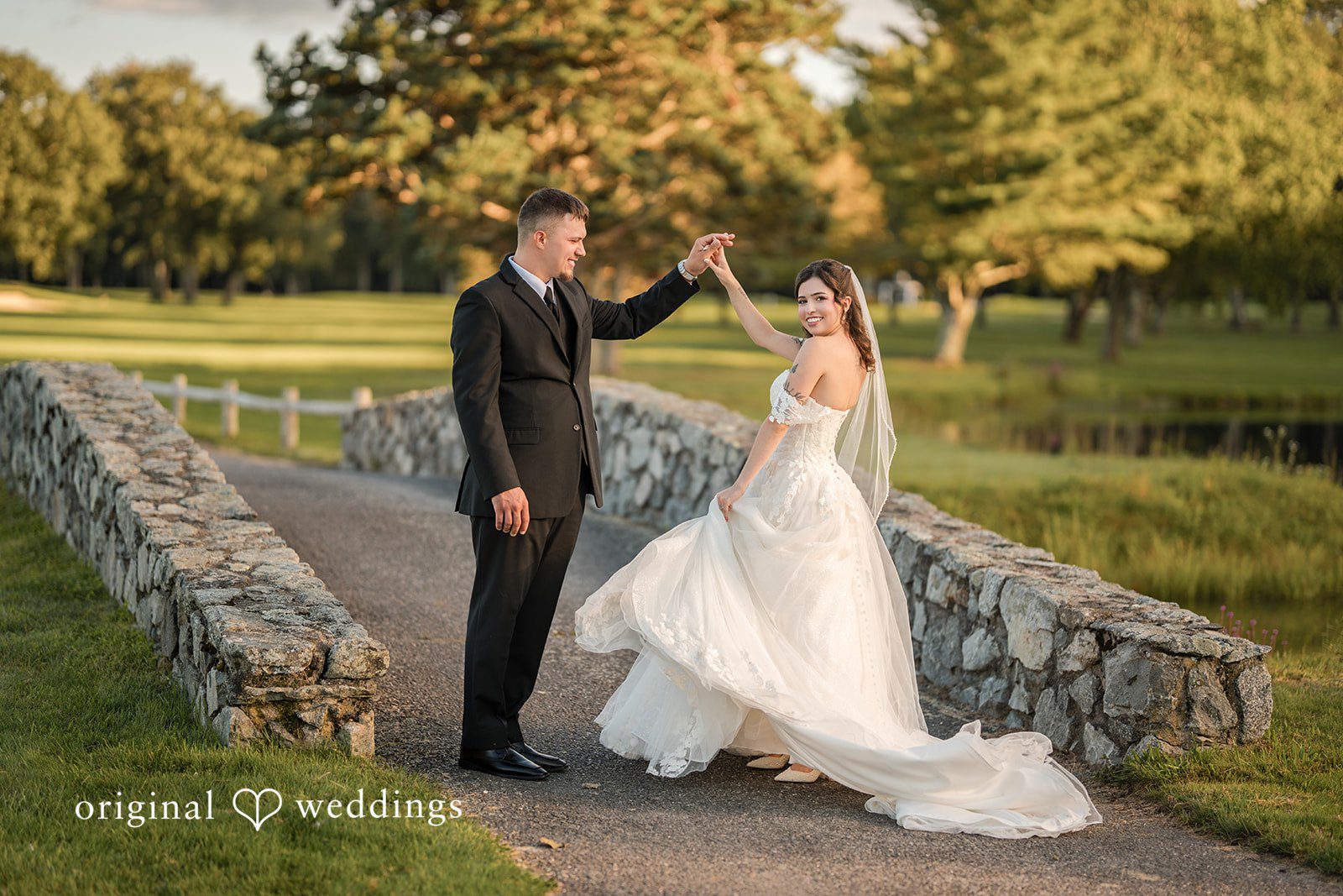 Emily + Angelo Bride and groom holding hands near a stone railing with a scenic backdrop.
