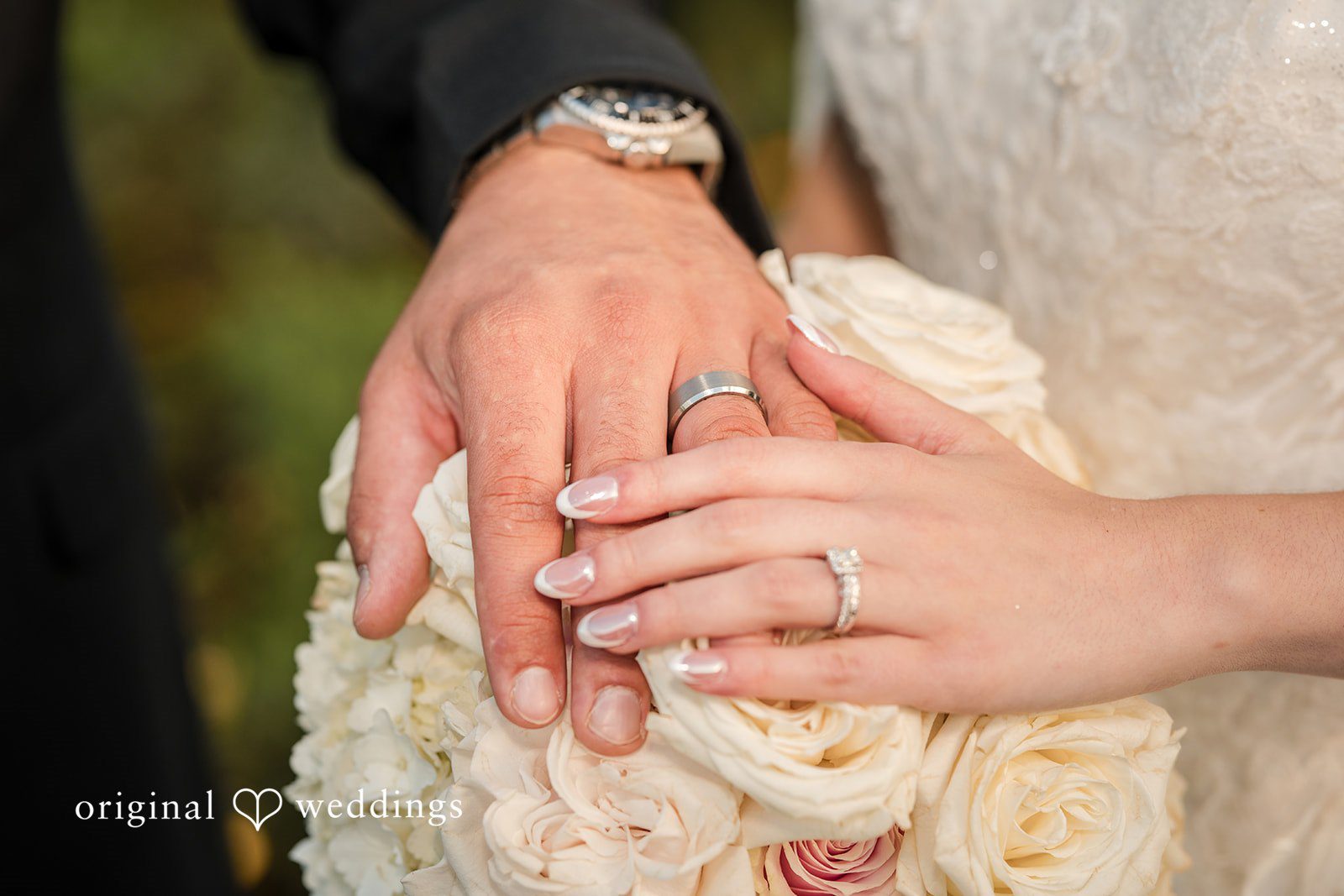 Emily + Angelo Close-up of a bride and groom's hands intertwined over a white floral bouquet.