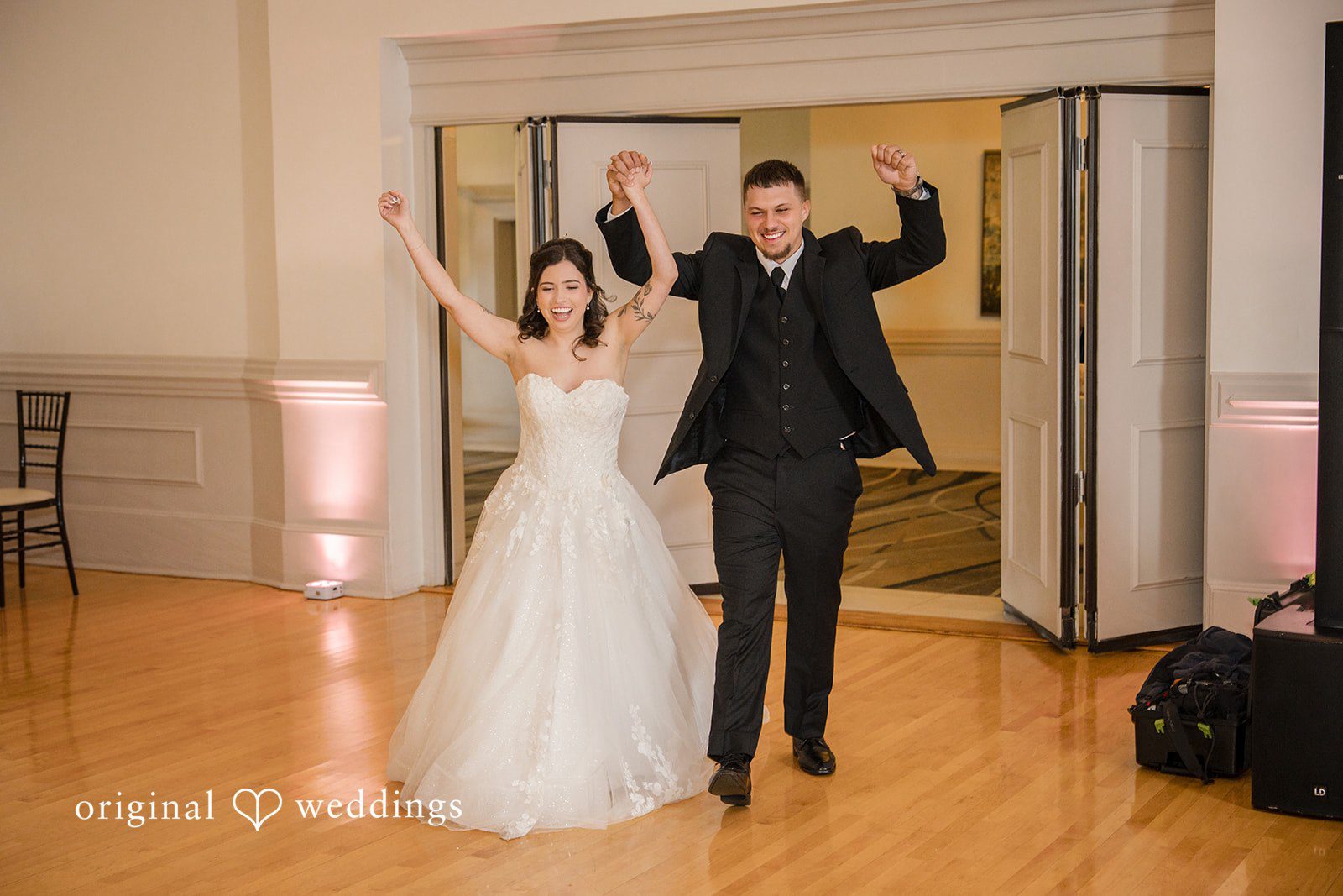 Emily + Angelo Bride and groom making their grand entrance into a reception hall with arms raised.