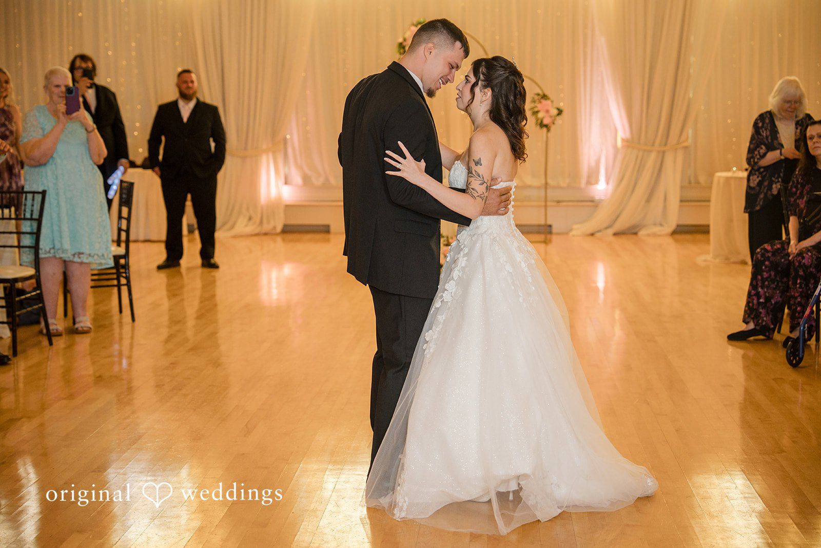 Emily + Angelo Bride and groom sharing their first dance together on a polished wooden floor.