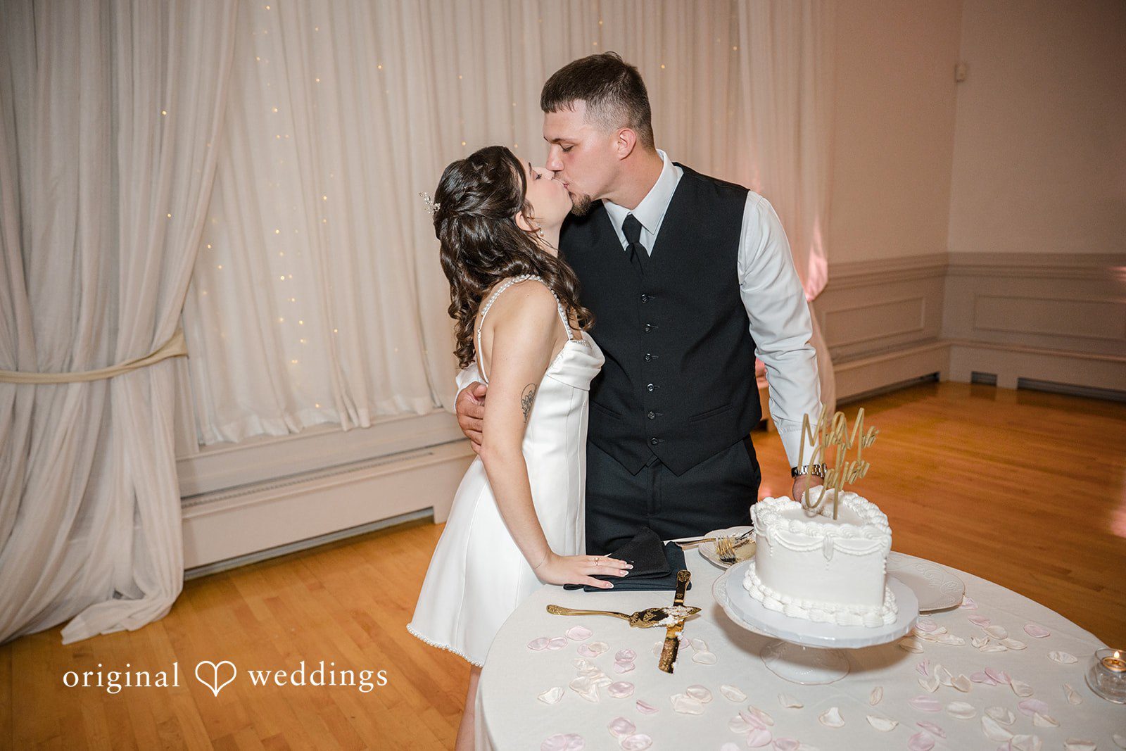 Emily + Angelo Bride and groom standing next to their tiered wedding cake during the reception.