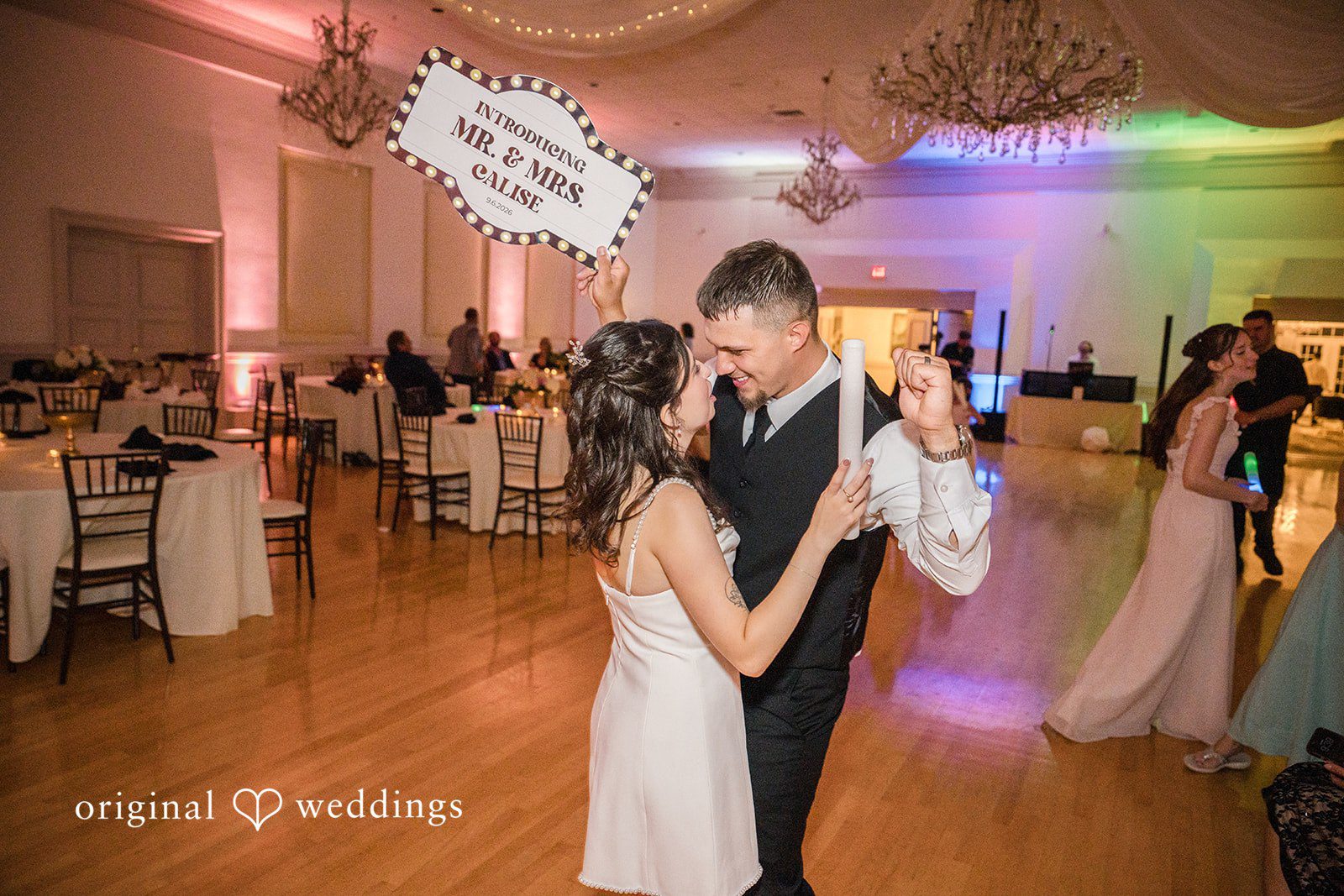 Emily + Angelo Bride and groom dancing together under colorful reception lights.