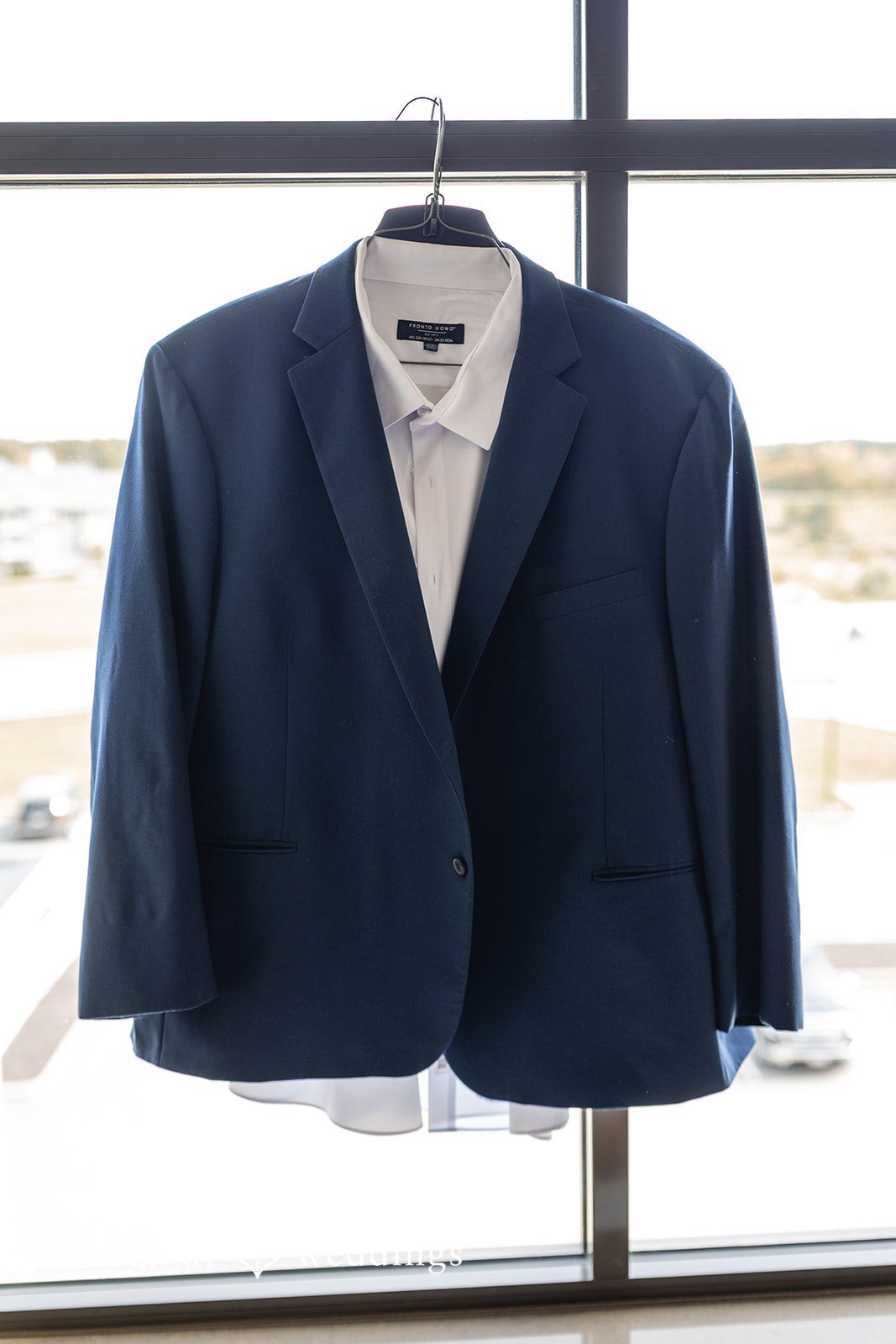 Groom's navy suit jacket hanging by the window