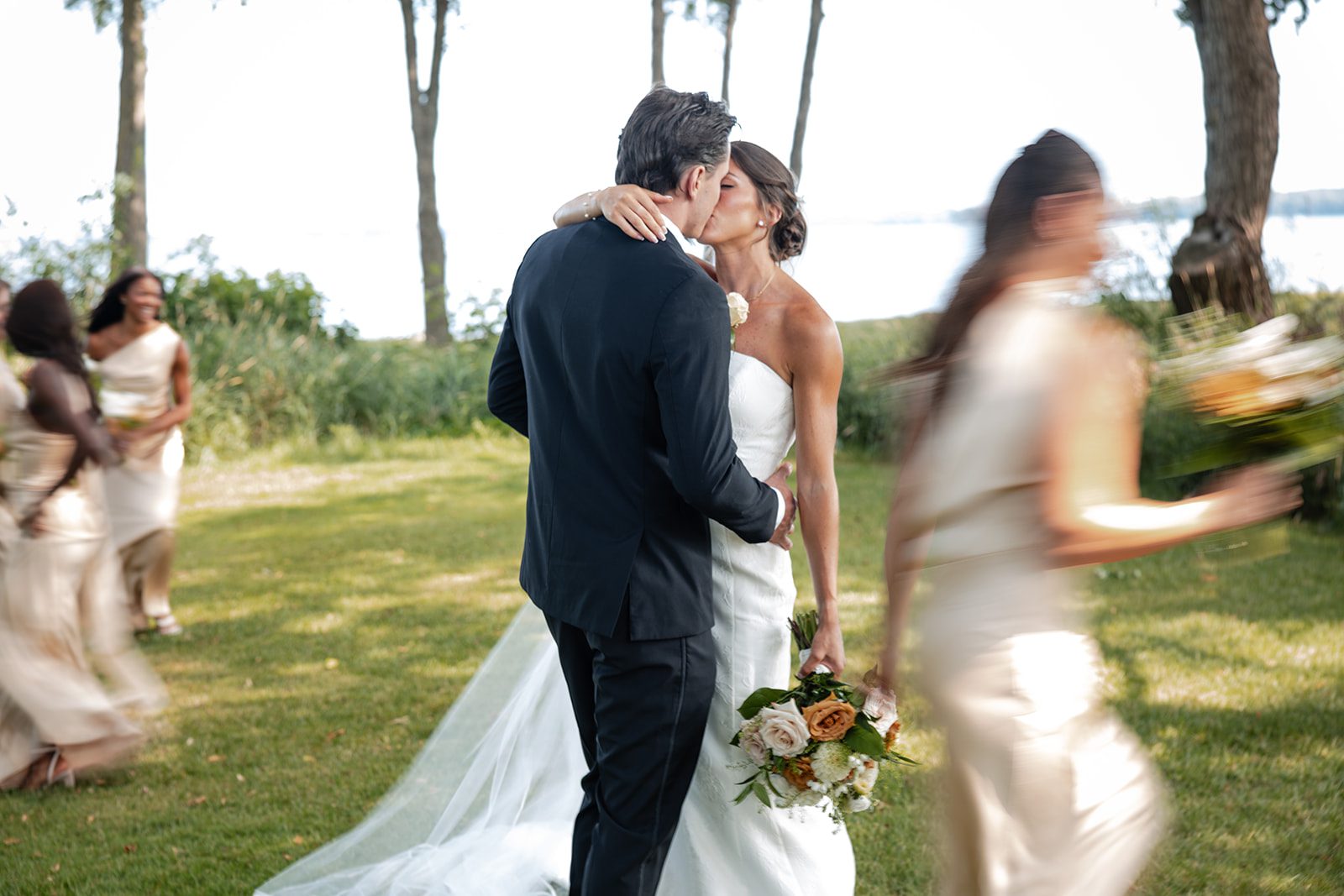 bishops-bay-country-club-timeless-madison-bianca-colin-p033-01 Newlyweds sharing a kiss with friends nearby