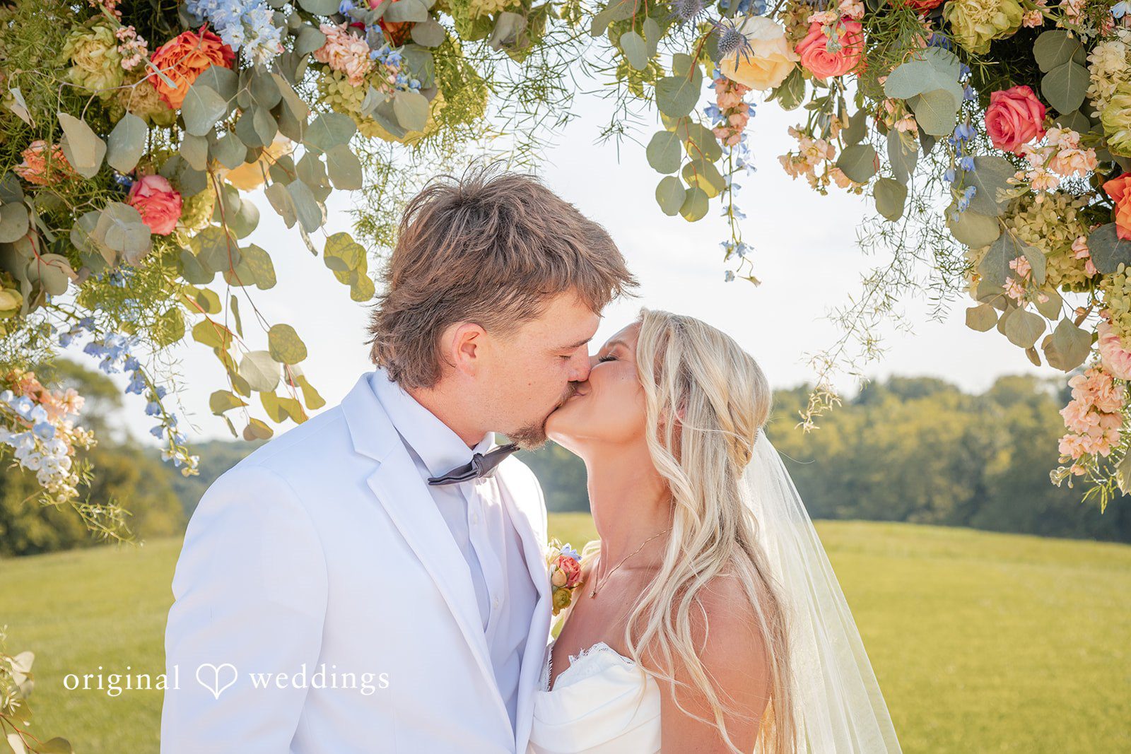 Couple sharing a kiss under the floral arch, captured by Cincinnati wedding photographers from Original Weddings