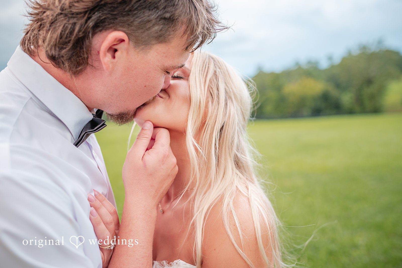 Groom kissing the bride with green fields behind