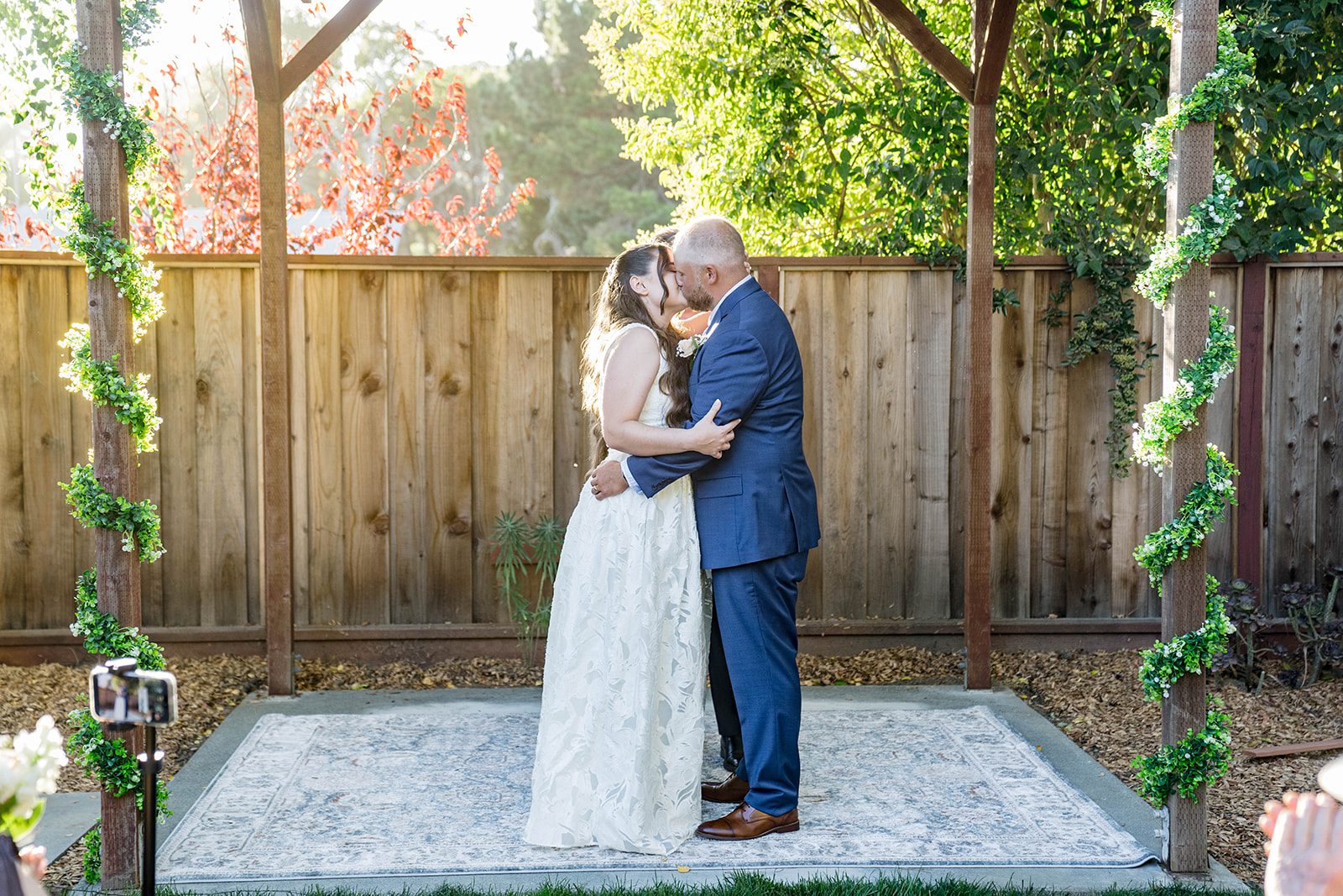 First kiss under the floral arch at a California backyard wedding