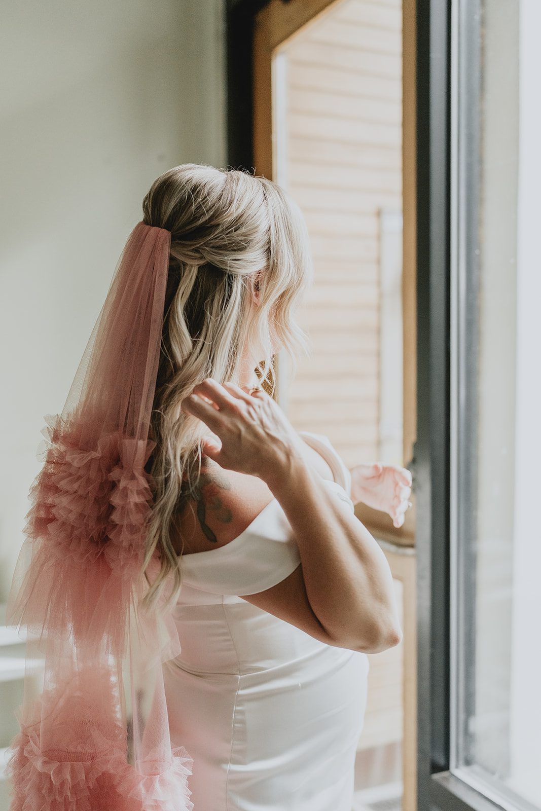 Bride adjusting her pink veil by the window