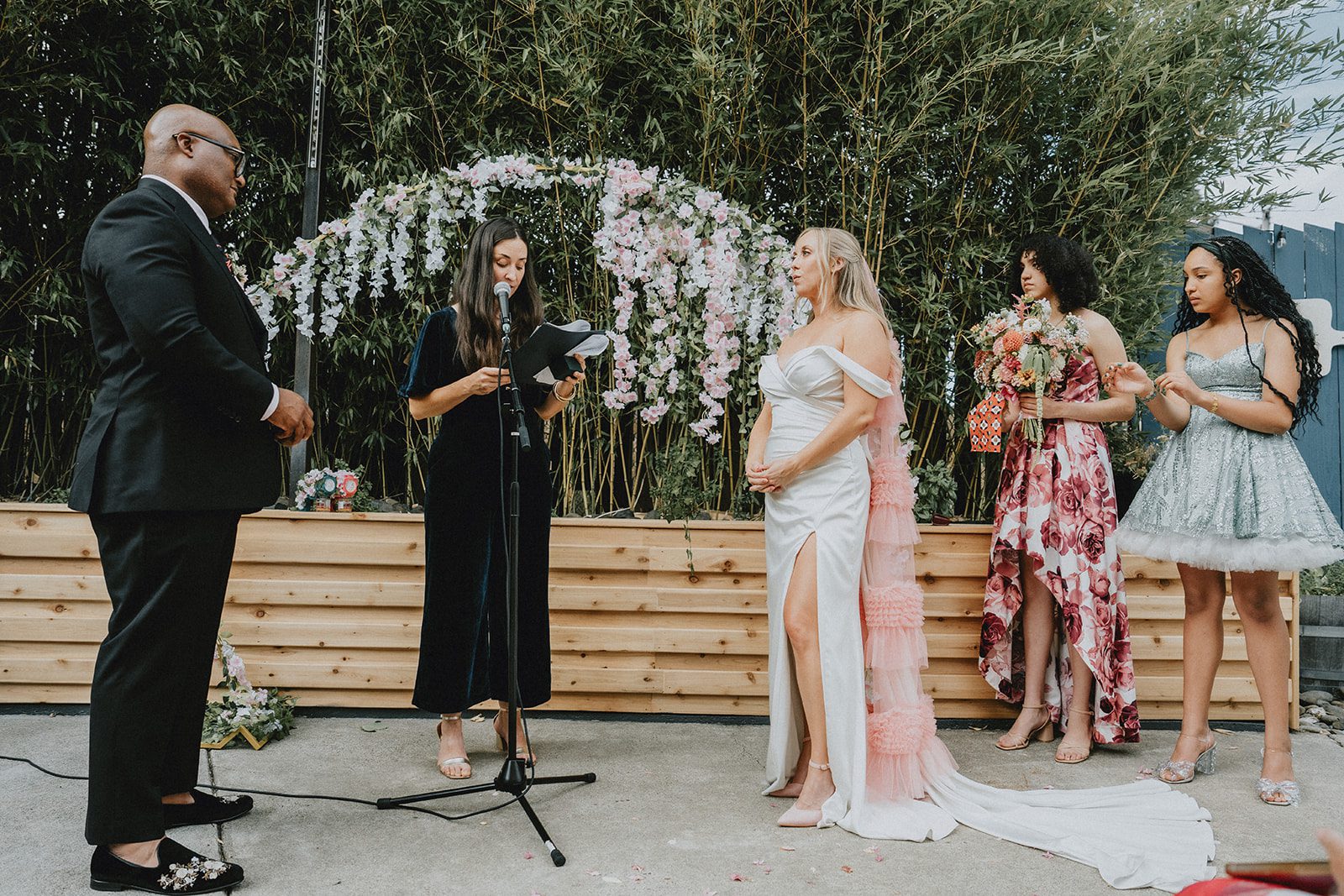 Officiant leading the outdoor ceremony under the floral arch