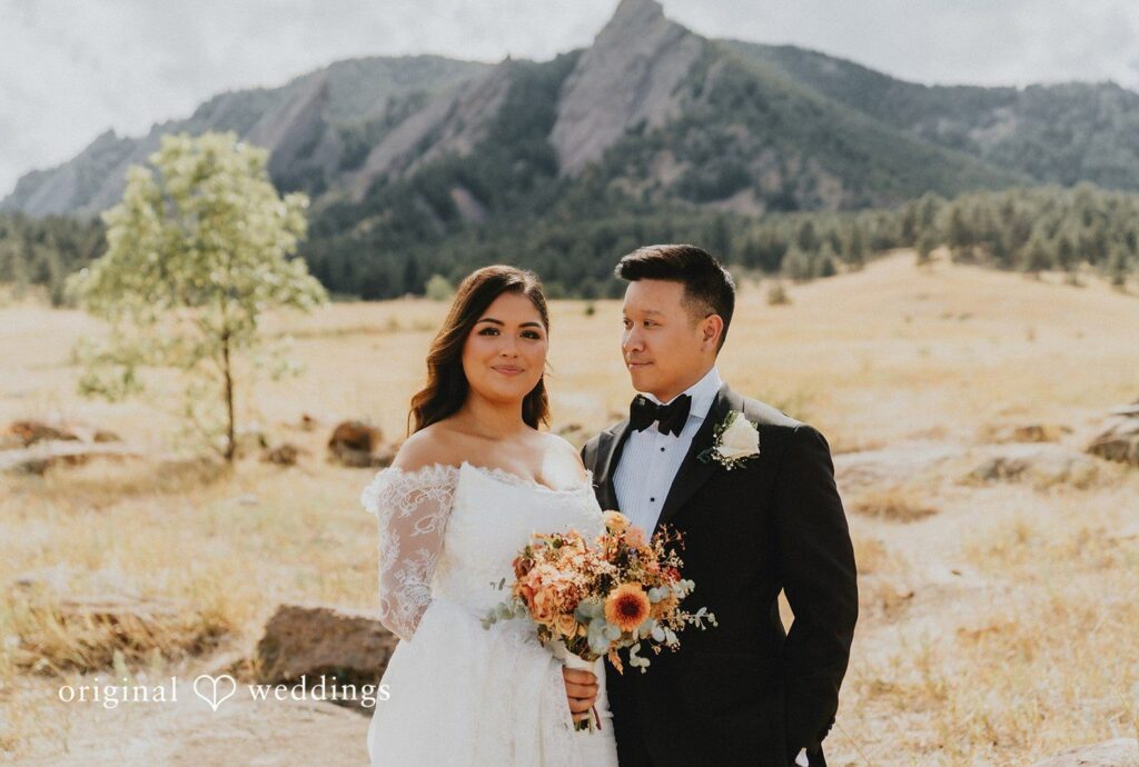 Church Ranch Event Center Wedding | Sonia & Michael 3 Bride and groom standing in a golden meadow with the Flatirons behind them, captured by Denver wedding photographers from Original Weddings at Church Ranch Event Center