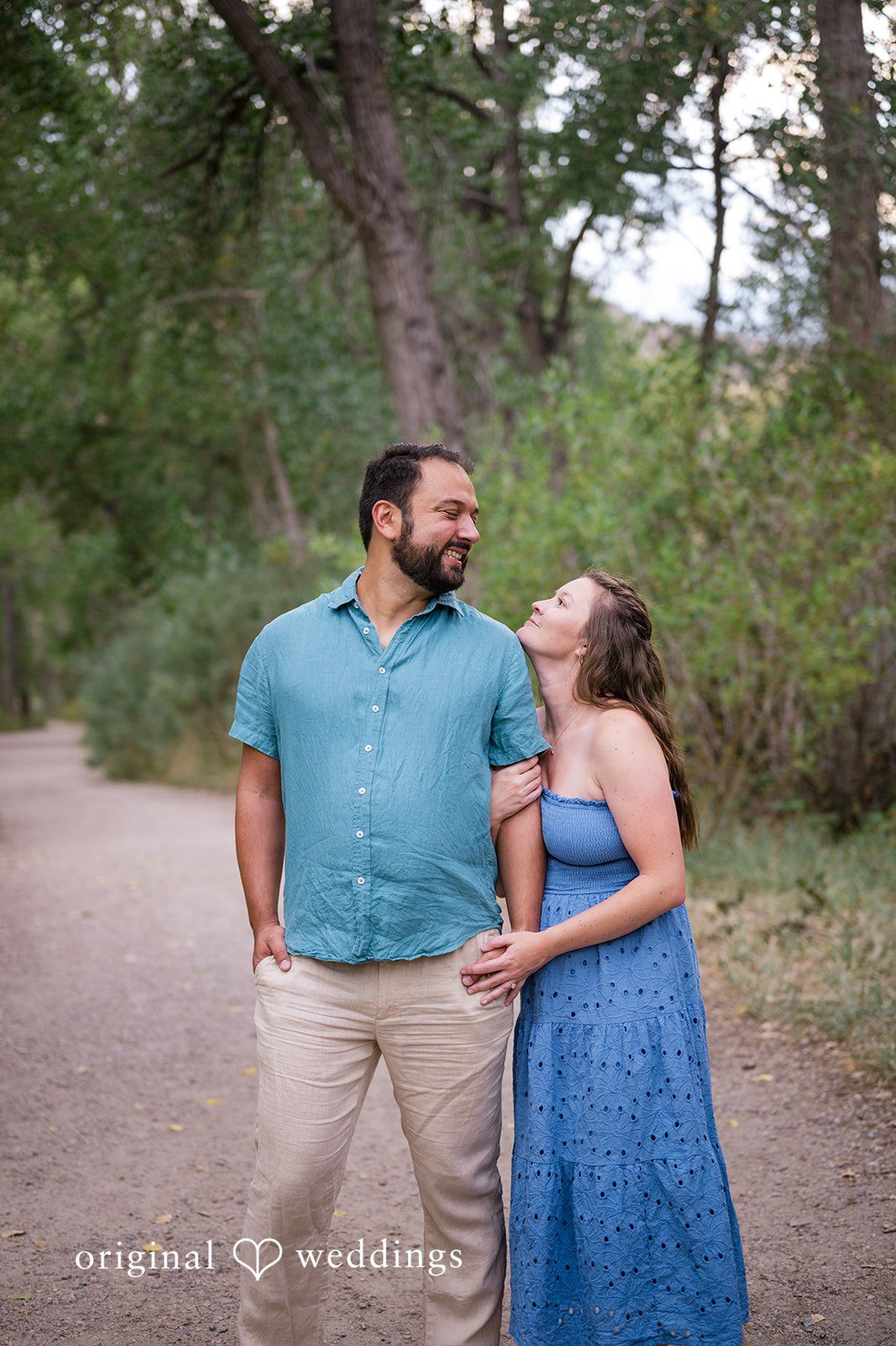 Theodore + Kathryn A man in a blue shirt and a woman in a long blue dress holding hands while walking through a forest.