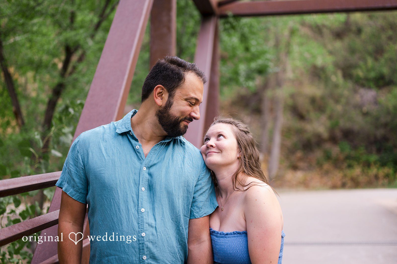 Theodore + Kathryn A man in a blue button-down shirt and a woman in a blue top smiling together on a pathway.