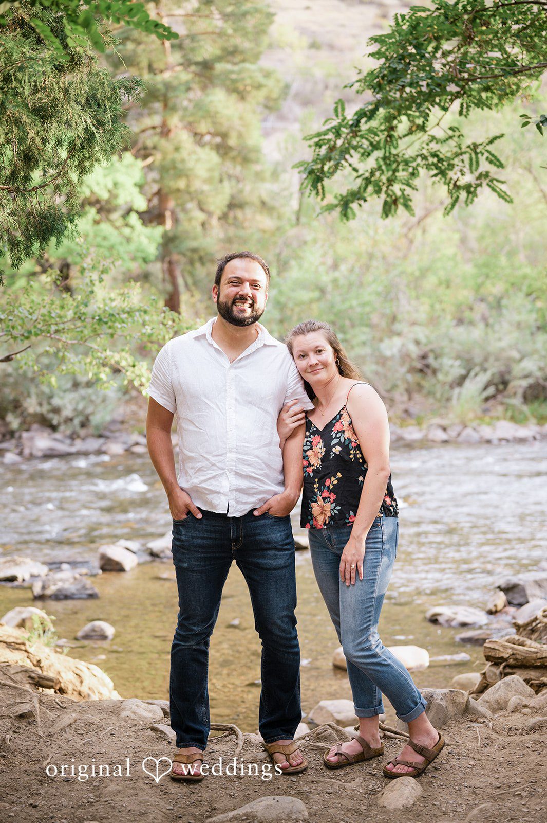 Theodore + Kathryn A man in a white tee and a woman in a patterned tank top smiling while standing near a stream.