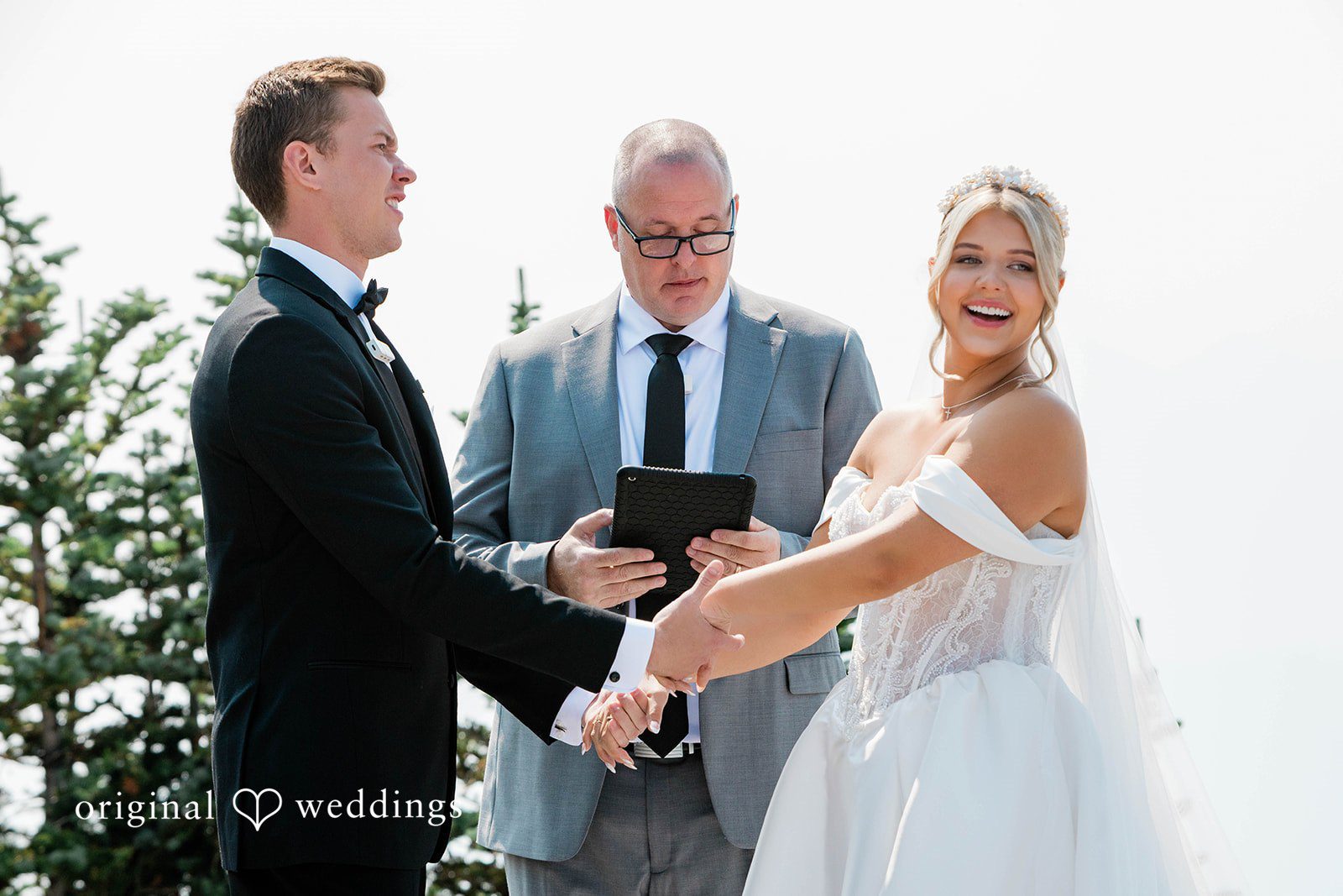 Bethany + Ryan A bride and groom hold hands while facing the wedding officiant during the ceremony.