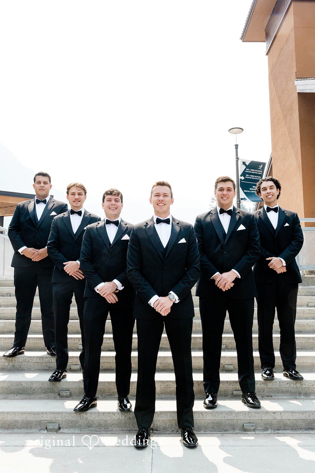 Bethany + Ryan A groom poses alongside a lineup of six groomsmen in matching black tuxedos.