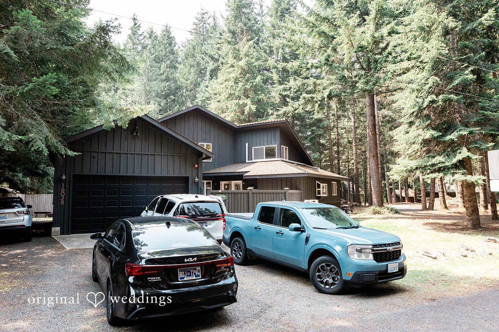 Bethany + Ryan Several vehicles are parked outside a rustic wooden cabin surrounded by trees.