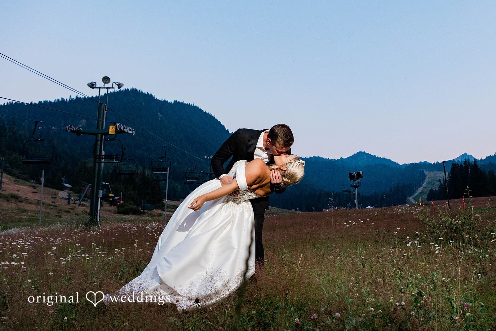 Bethany + Ryan A groom dips a bride while posing on a mountain slope at dusk.