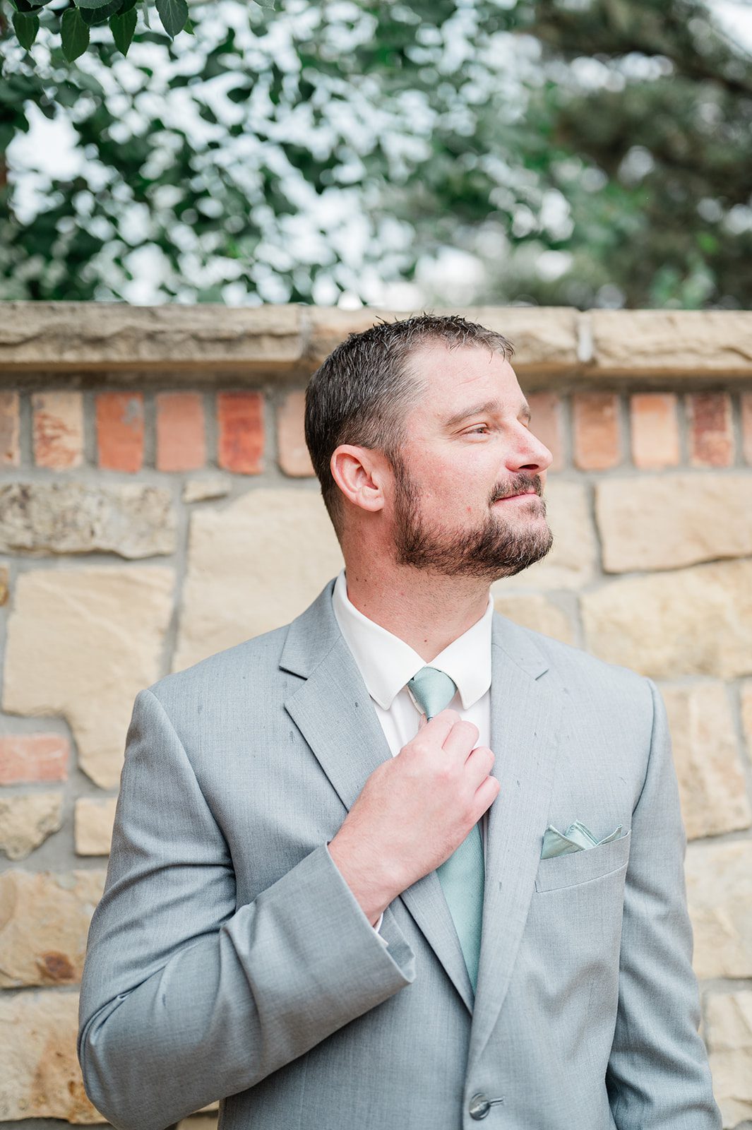 Groom adjusting his tie in a light gray suit