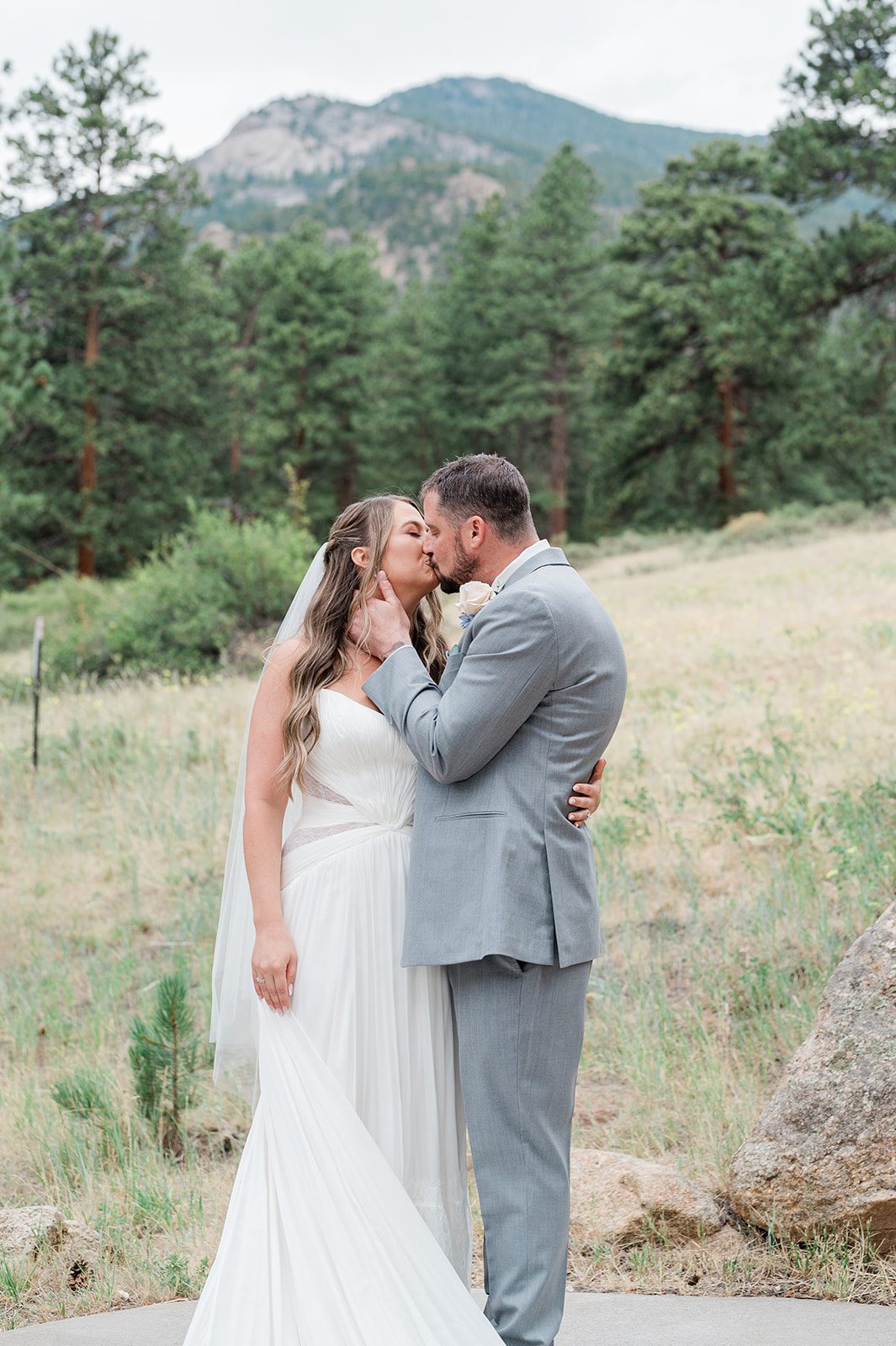 Newlyweds kissing in a field with mountain views