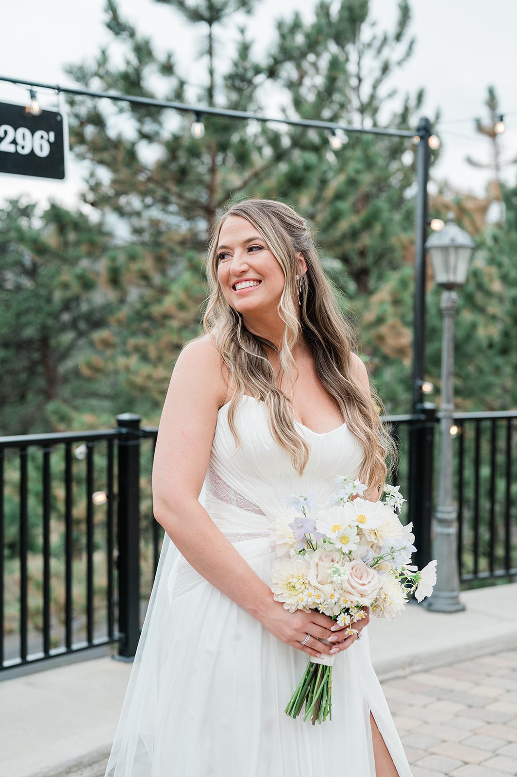 Bride smiling with her bouquet surrounded by pine trees