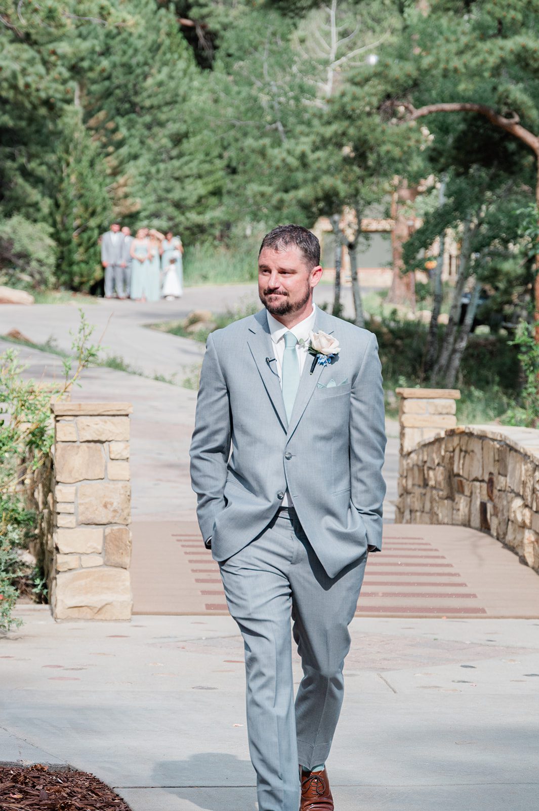 Groom in a light gray suit walking along a stone path